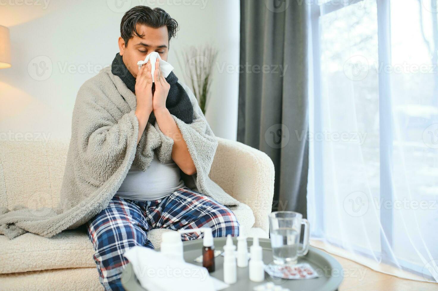 Portrait of sick Indian man with runny nose holding paper napkins near face sitting at home. Flu, virus, allergy concept photo