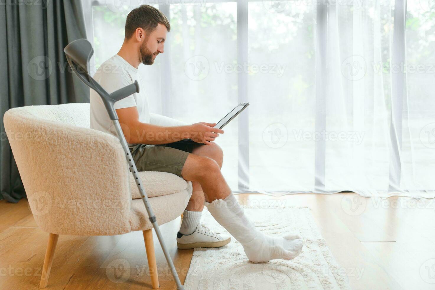 Happy young man with arm in a cast sitting on the couch at home and communicating on a laptop photo