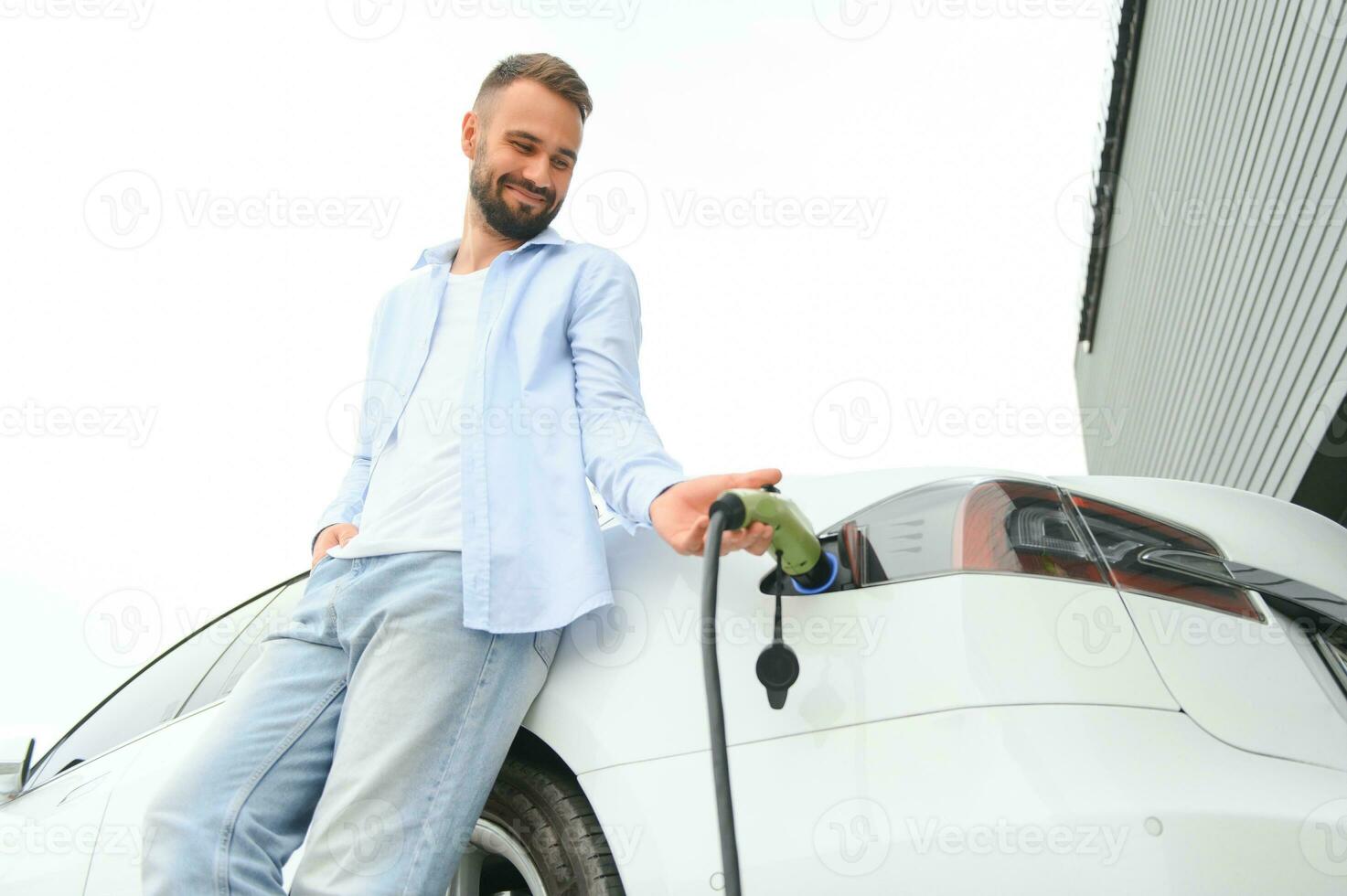 Stylish man inserts plug into the electric car charging socket photo