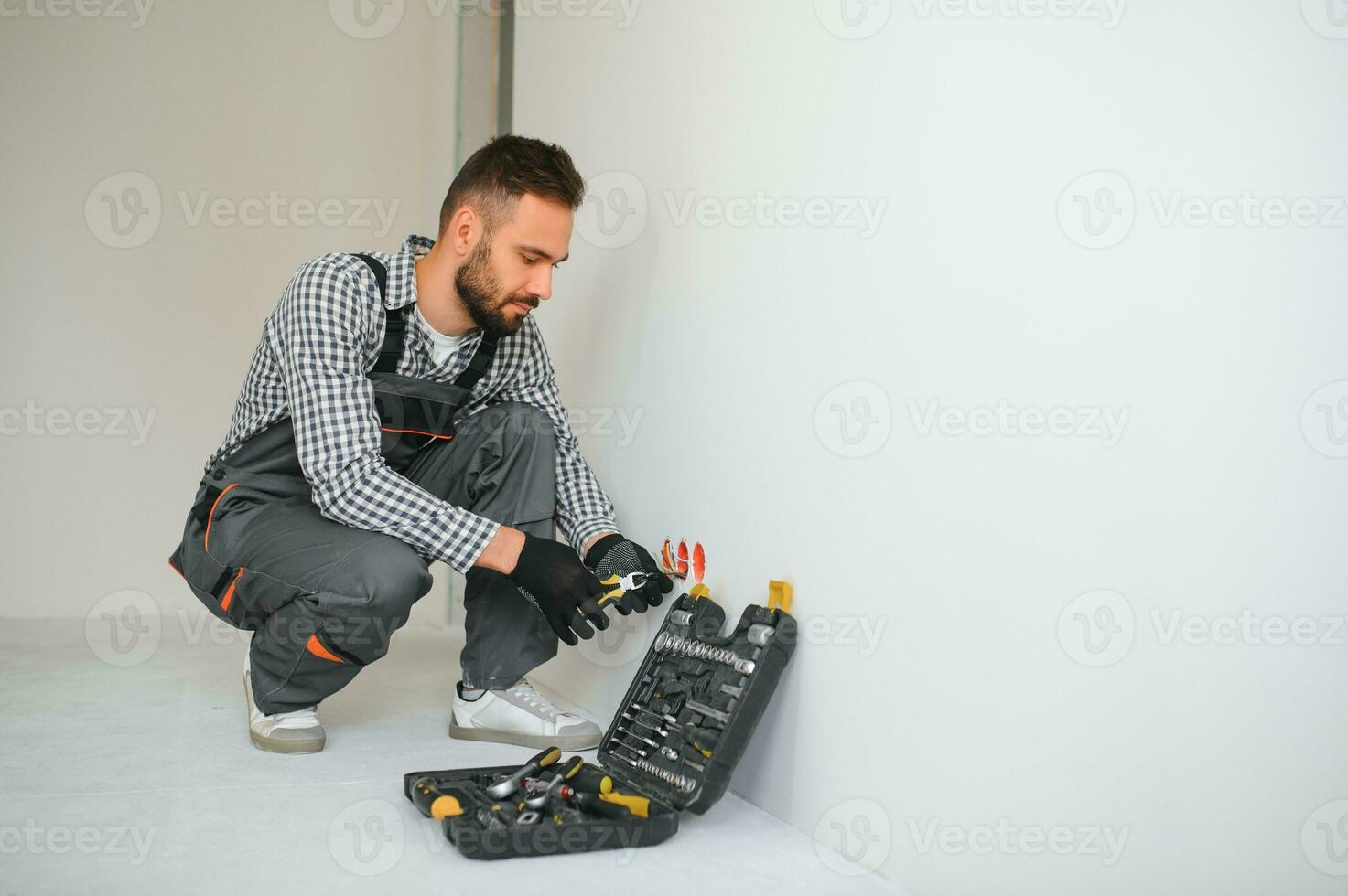 Electrician in uniform mounting electric sockets on the white wall indoors photo