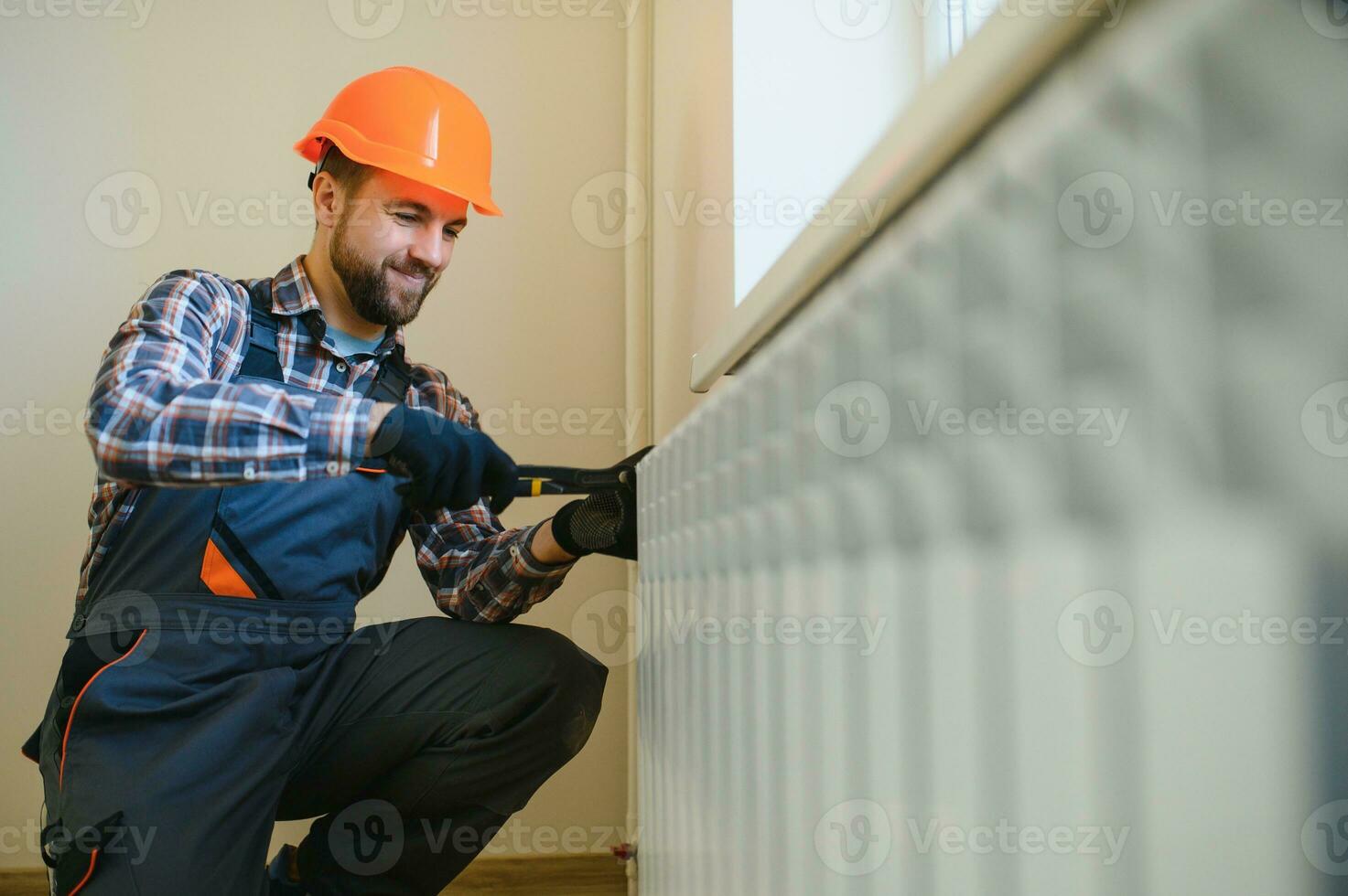 young man plumber checking radiator while installing heating system in apartment photo