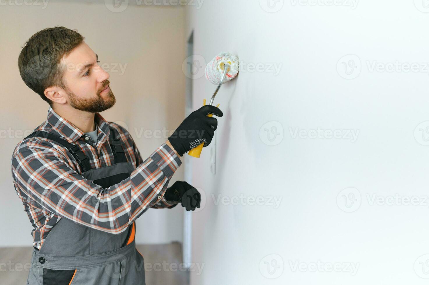 Painter painting a wall with paint roller. Builder worker painting surface with white color photo