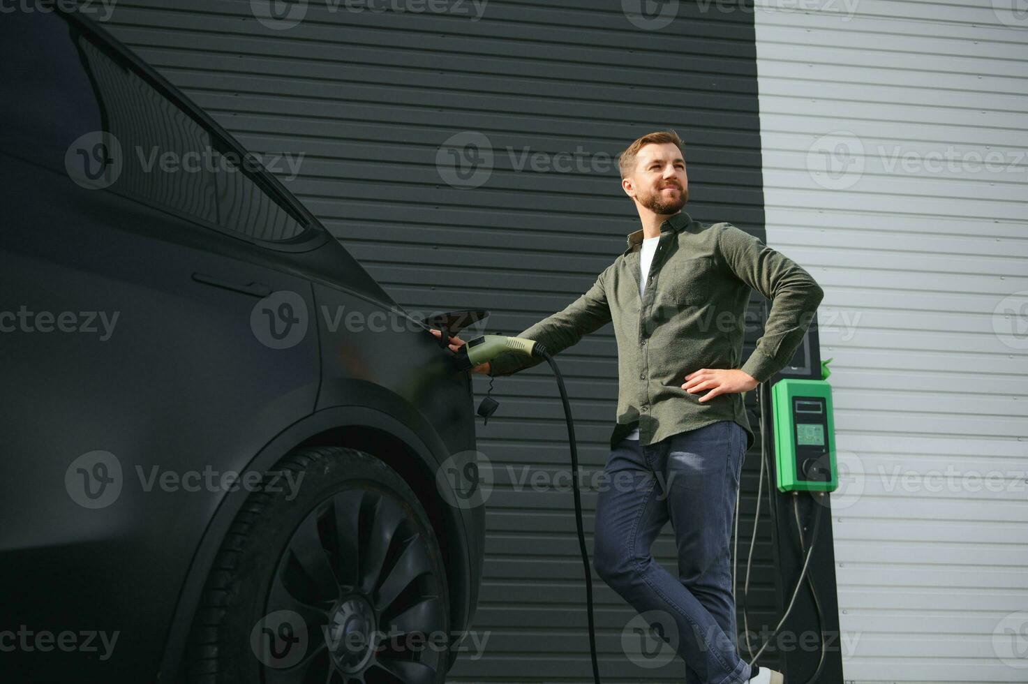 un hombre soportes cerca un cargando estación y cargos su eléctrico coche foto