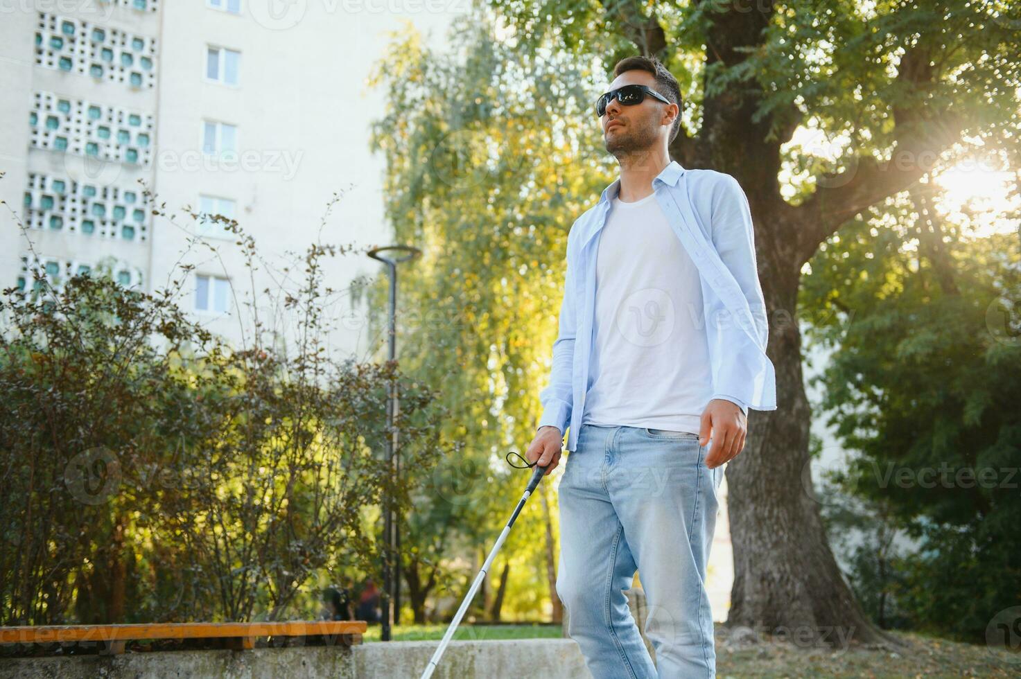 Young handsome blinded man walking with stick in town photo