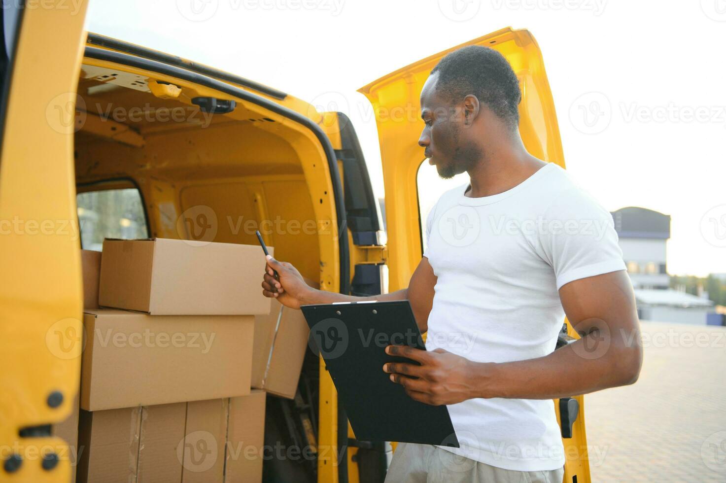 african male postal delivery courier man in front of car delivering package photo