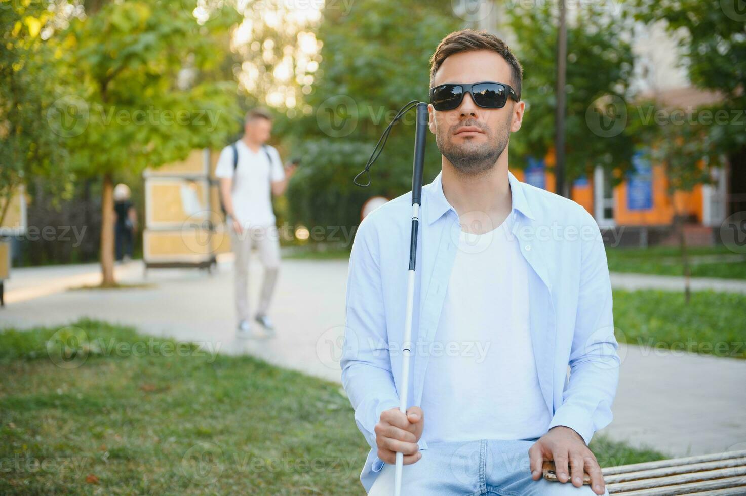 Blind man with a walking stick sitting on a bench at a park photo