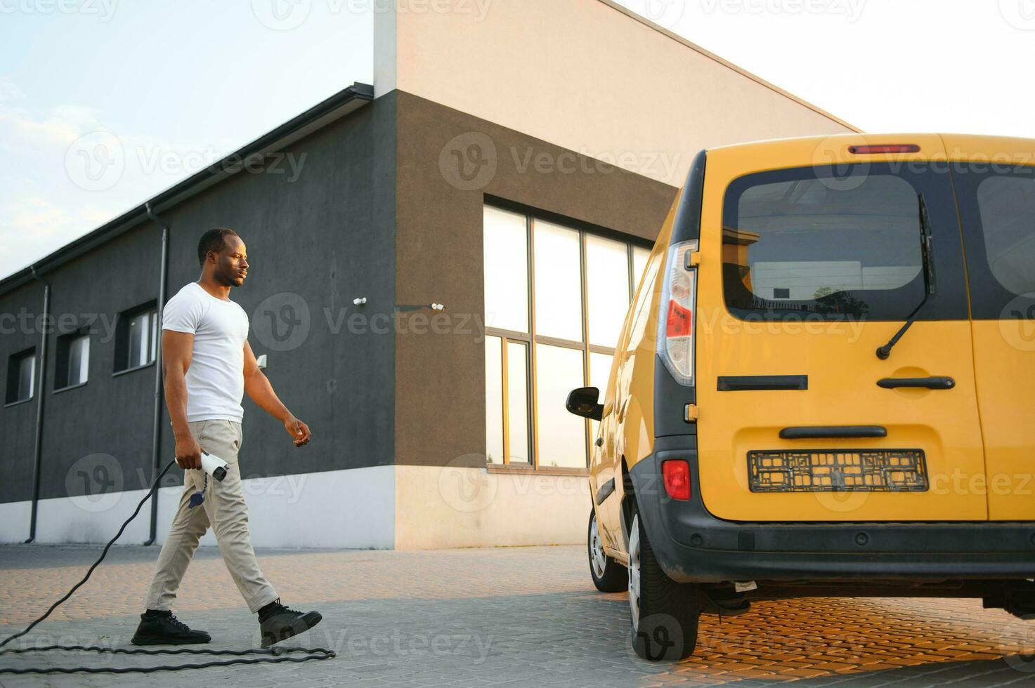 african man holding charge cable in on hand standing near electric car. photo