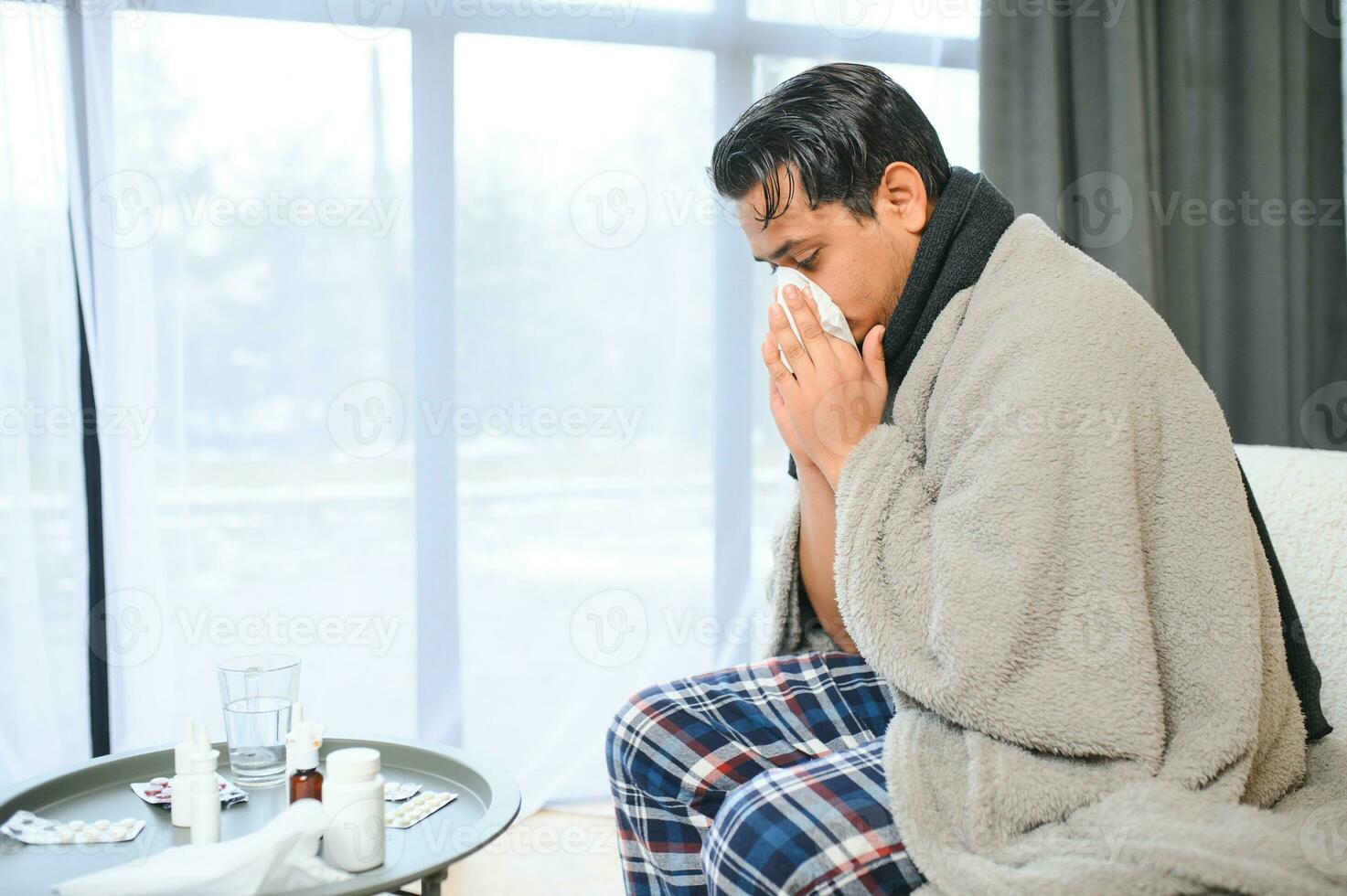 Portrait of sick Indian man with runny nose holding paper napkins near face sitting at home. Flu, virus, allergy concept photo