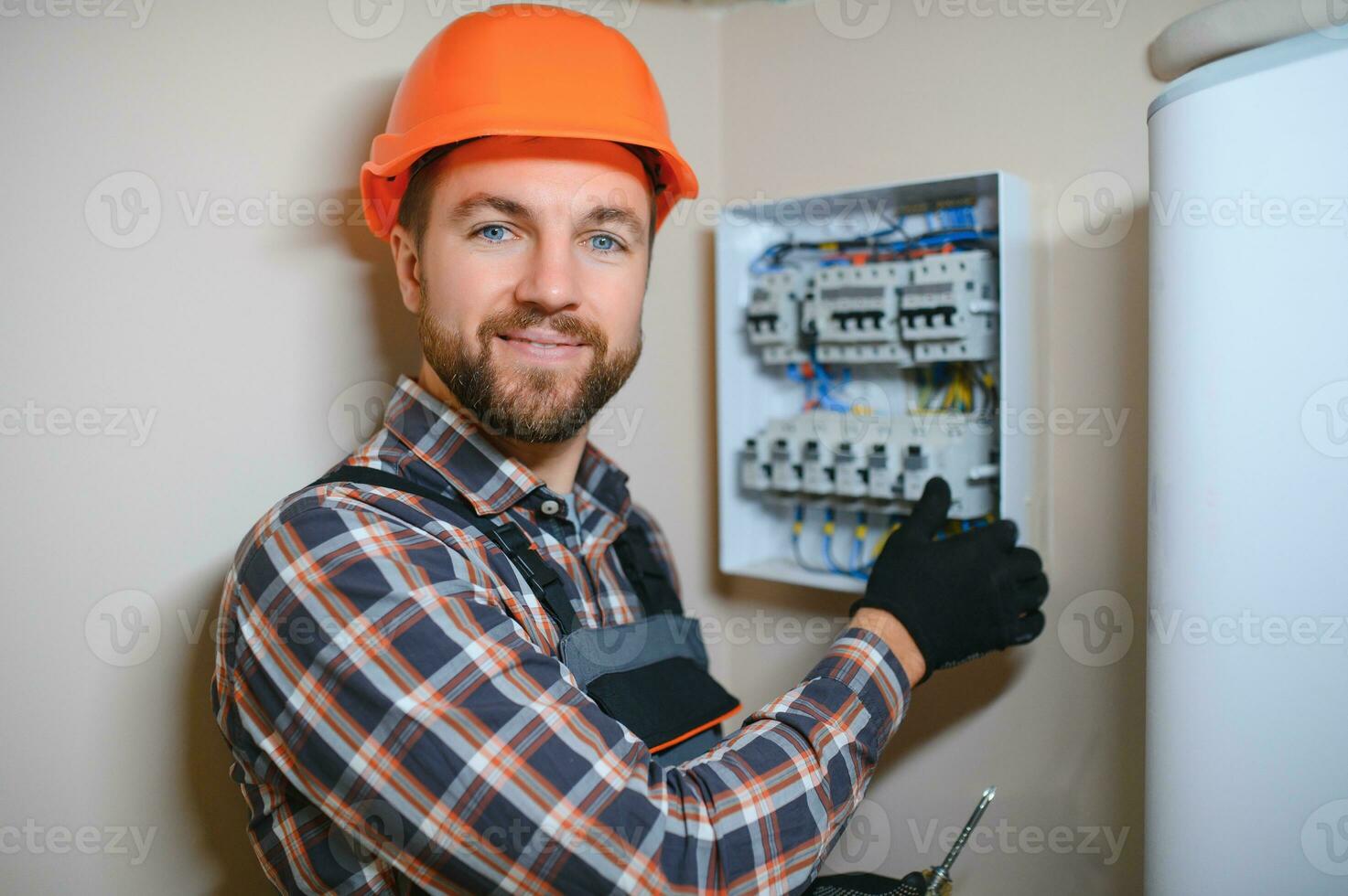 un masculino electricista trabajos en un tablero de conmutadores con un eléctrico conectando cable foto