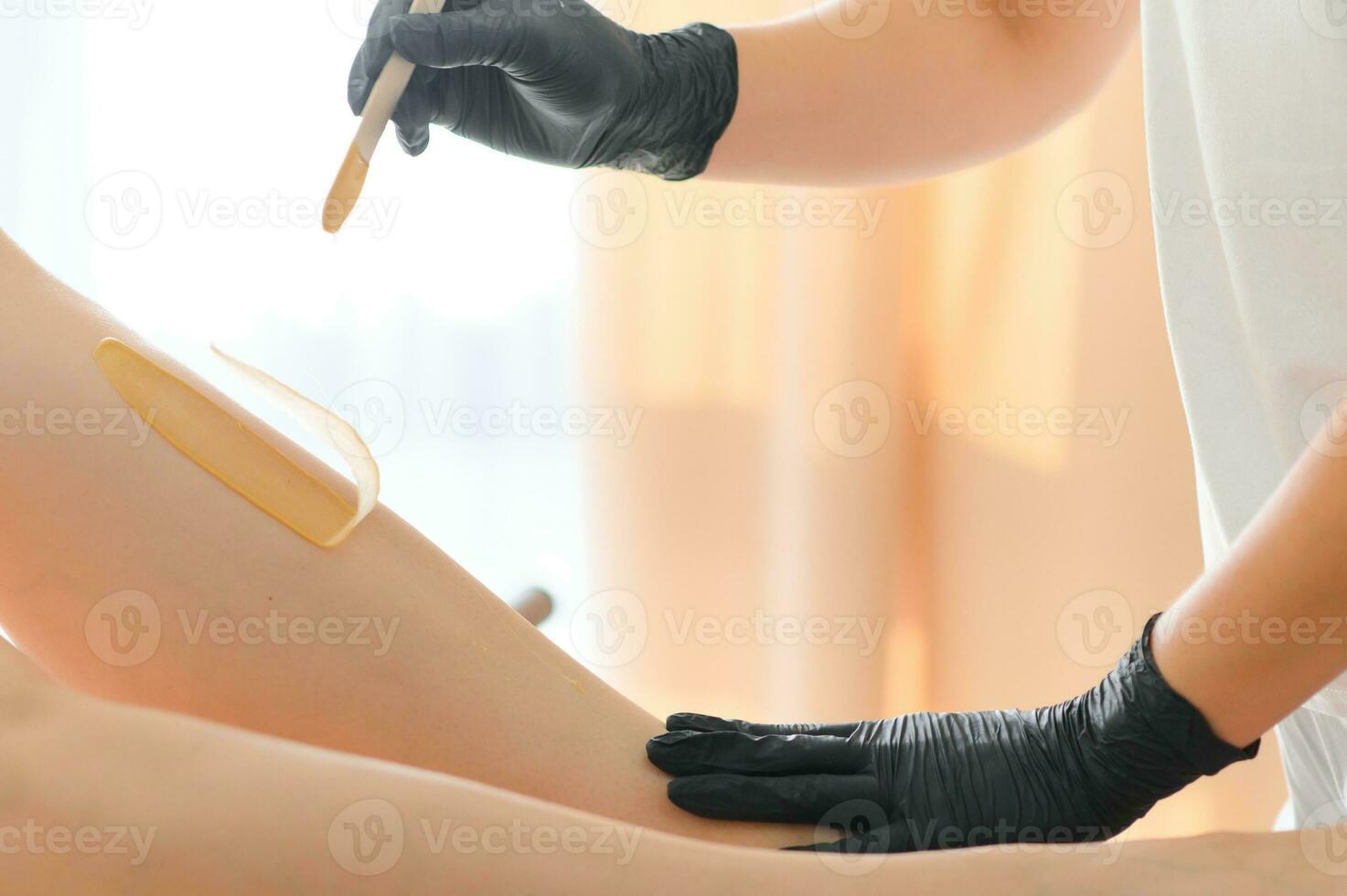 Young woman depilating legs with liquid sugar in spa center photo