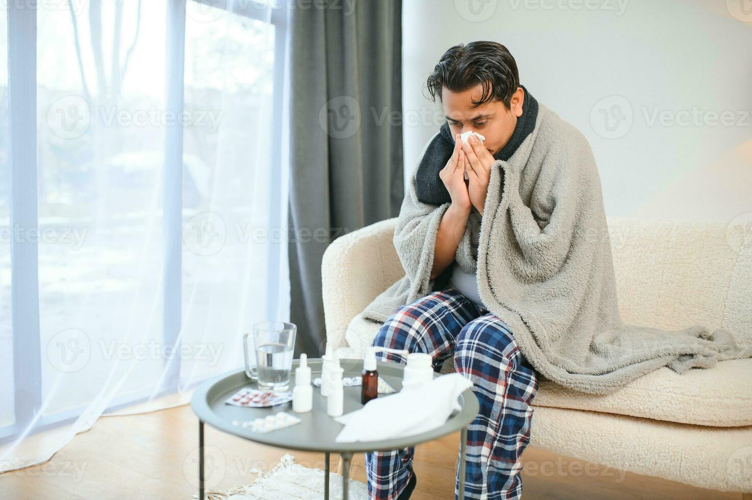 Portrait of sick Indian man with runny nose holding paper napkins near face sitting at home. Flu, virus, allergy concept photo