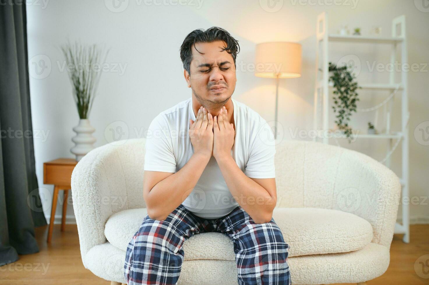 enfermo joven indio hombre sufrimiento garganta dolor mientras sentado en cama a hogar foto