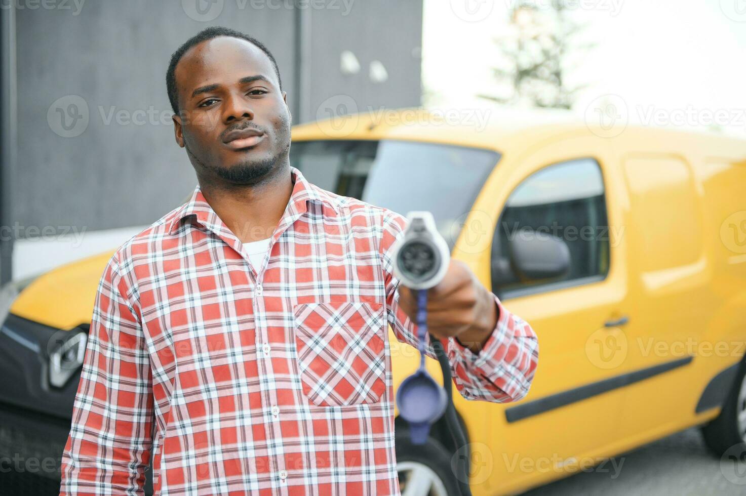 A african american man stands next to yellow electric delivery van at electric vehicle charging stations photo