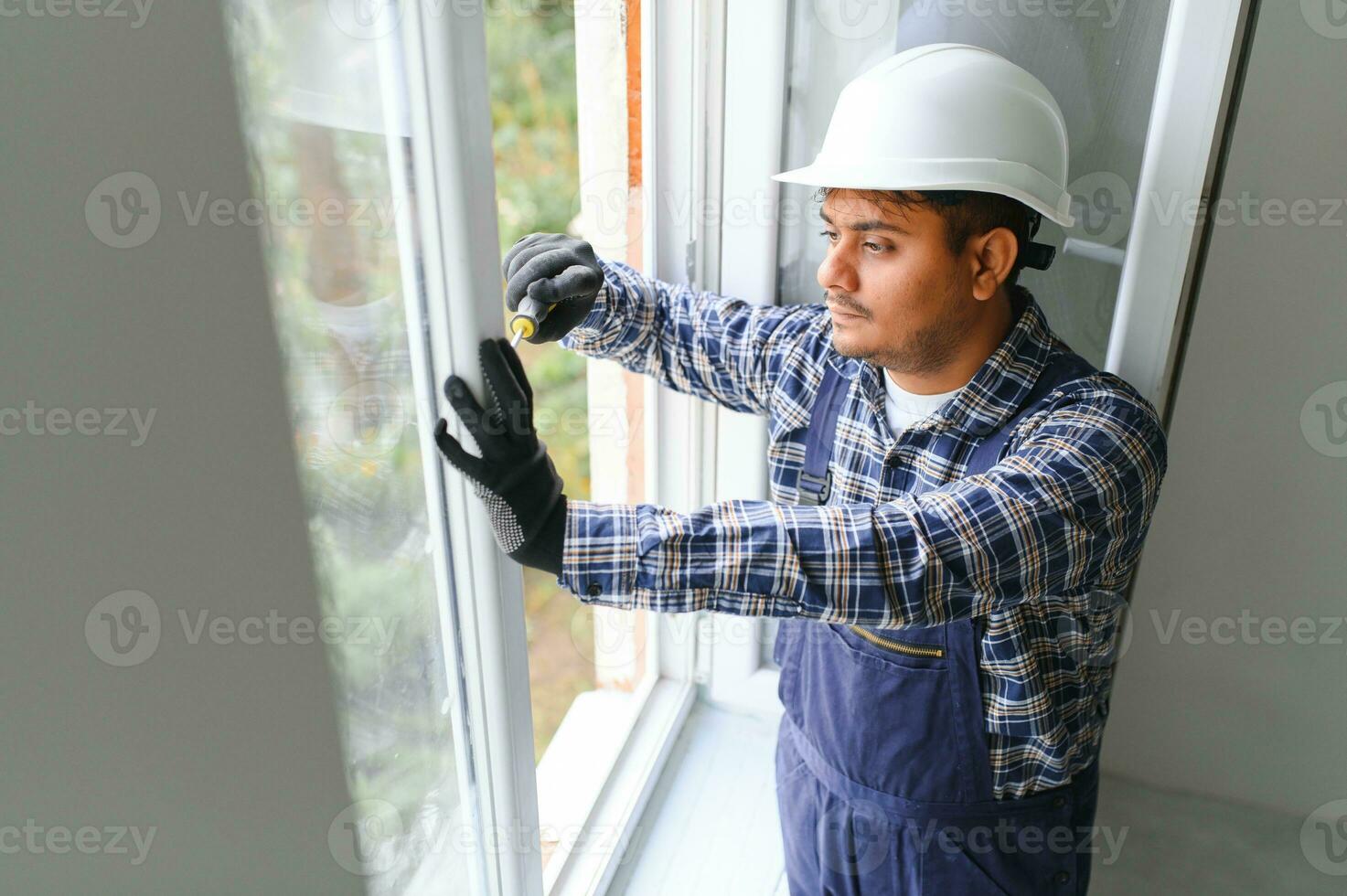 Indian Workman in overalls installing or adjusting plastic windows in the living room at home photo