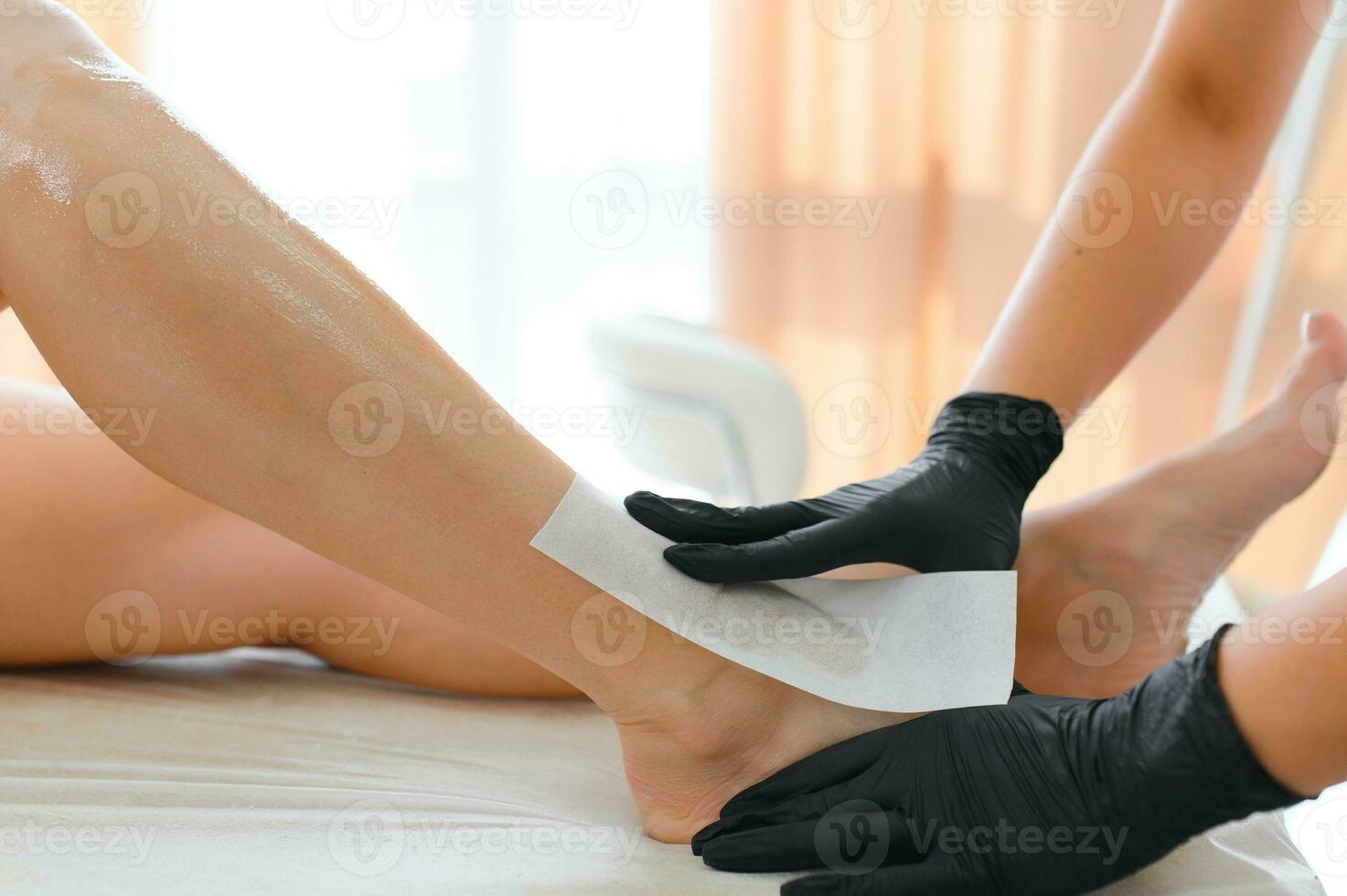 Beautician waxing female legs in spa center photo