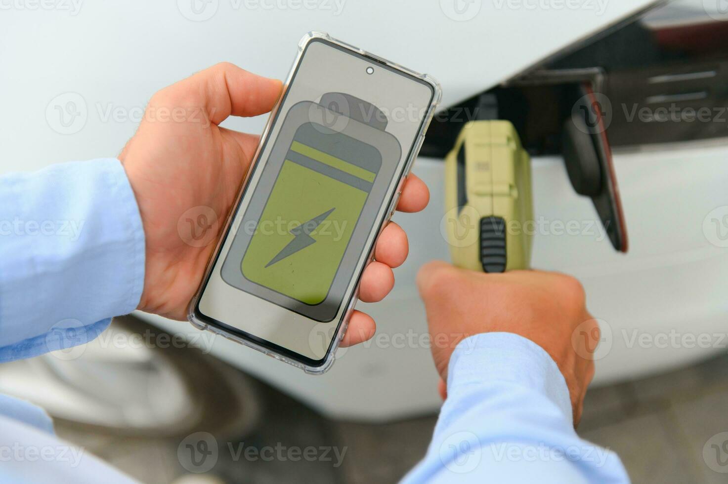 Casual man with smartphone near electric car waiting for the finish of the battery charging process photo