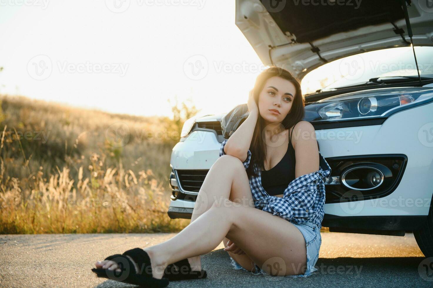 Beautiful young girl sitting at a broken car on the road desperate to get help photo