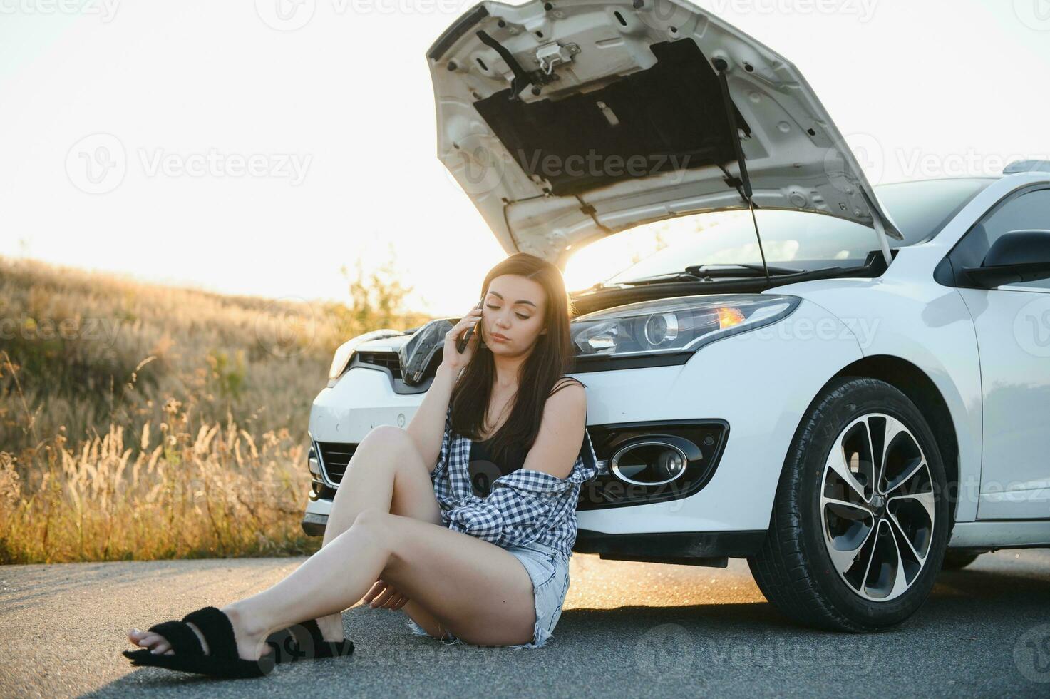 The young girl broke the car and she opened the hood and tried to repair the car on the road. A woman calls on a smartphone with a car evacuation service photo