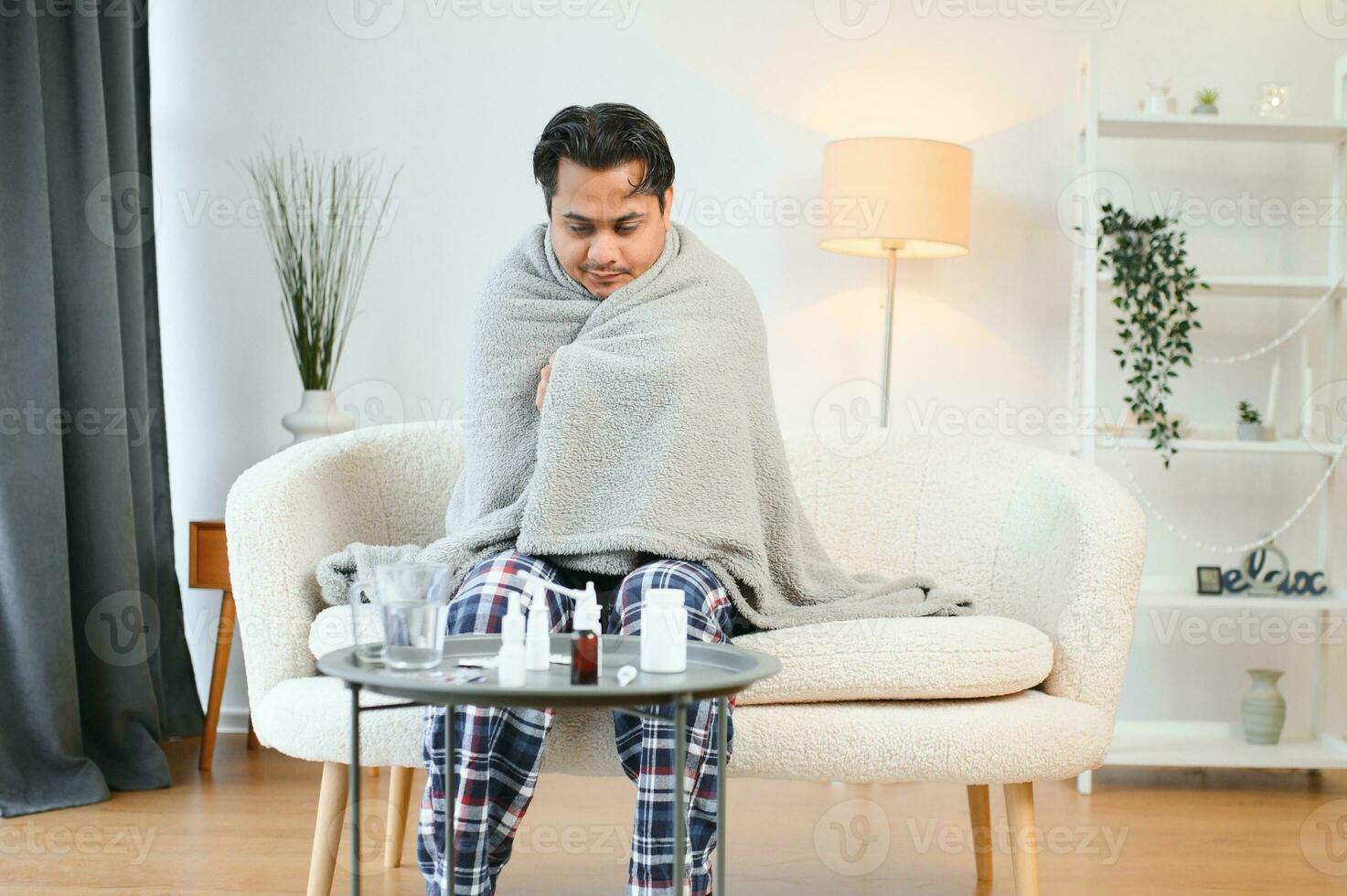 Sick Indian man in plaid sit alone shivering from cold. Unhealthy Arabian guy sit on chair feeling discomfort try to warming up photo