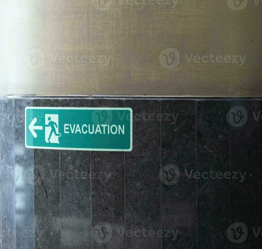 Selective fire exit sign on white ceiling. Green fire escape sign hanging on office wall. Fire fighting equipment concept. photo