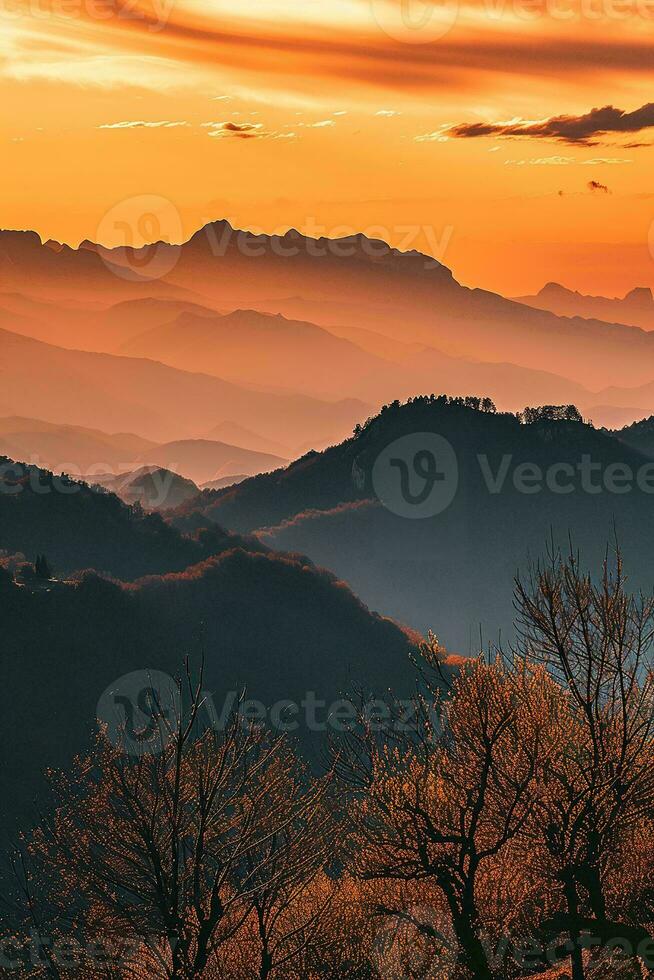 AI generated Breathtaking sunset illuminating a layered mountain landscape, with the orange hues casting silhouettes and highlighting the intricate shapes of bare trees. photo