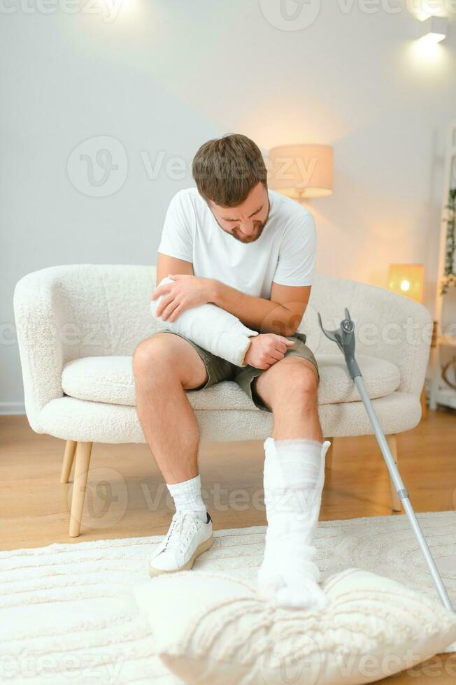 Recovery after physical injury in accident at home Sad unlucky young man with broken leg, injured arm photo