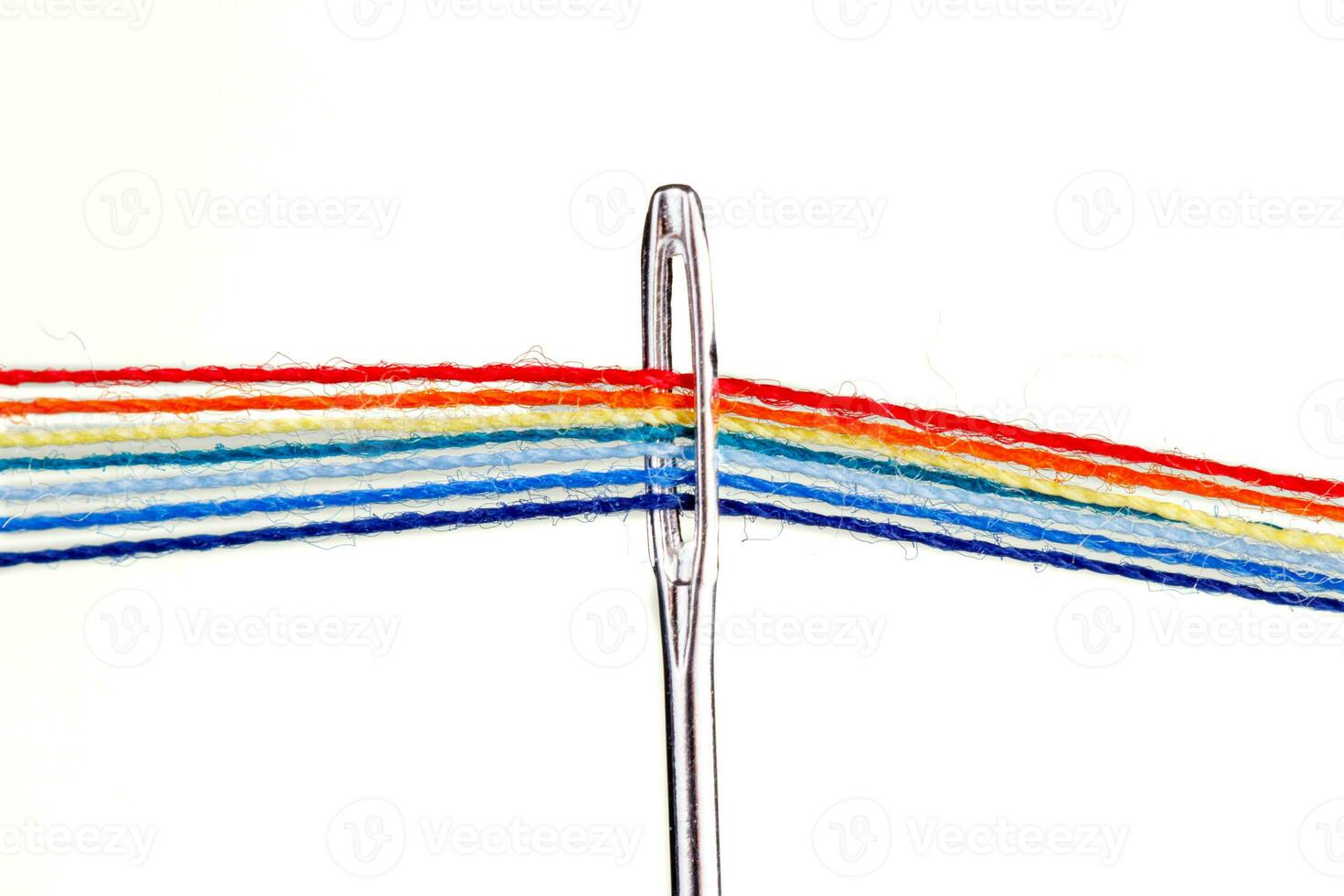 multi-colored threads for sewing in the form of a rainbow pass through an antique needle on a white background photo