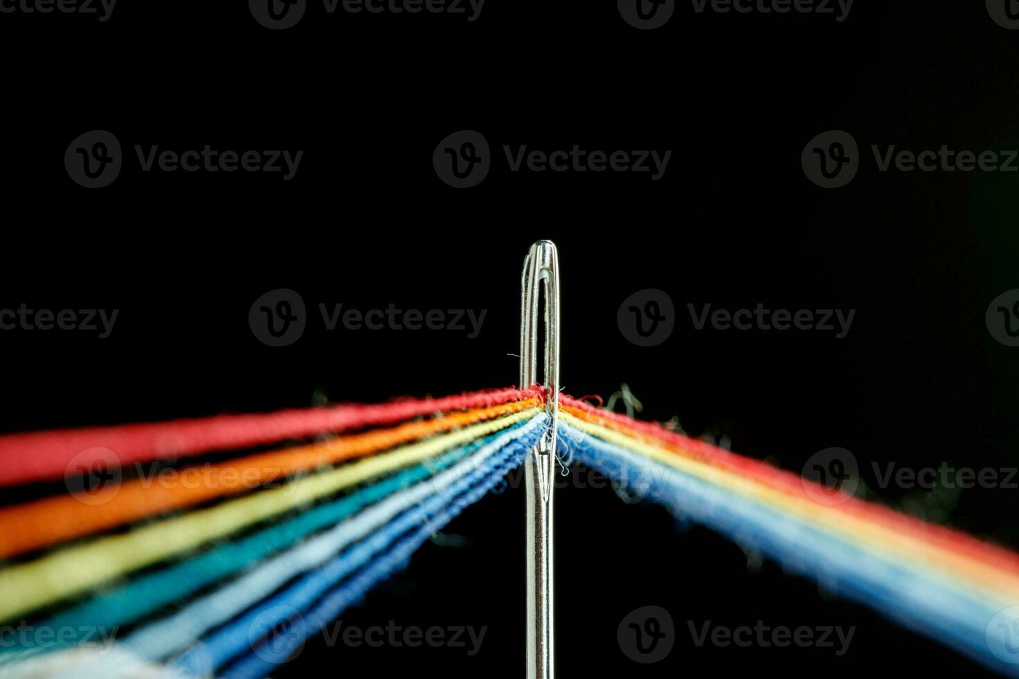 multi-colored threads for sewing in the form of a rainbow pass through an antique needle on a black background photo