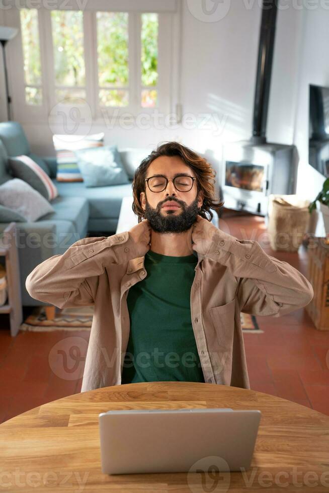 Man working with laptop from home stretching back to correct posture. Overworked Computer Concept. photo