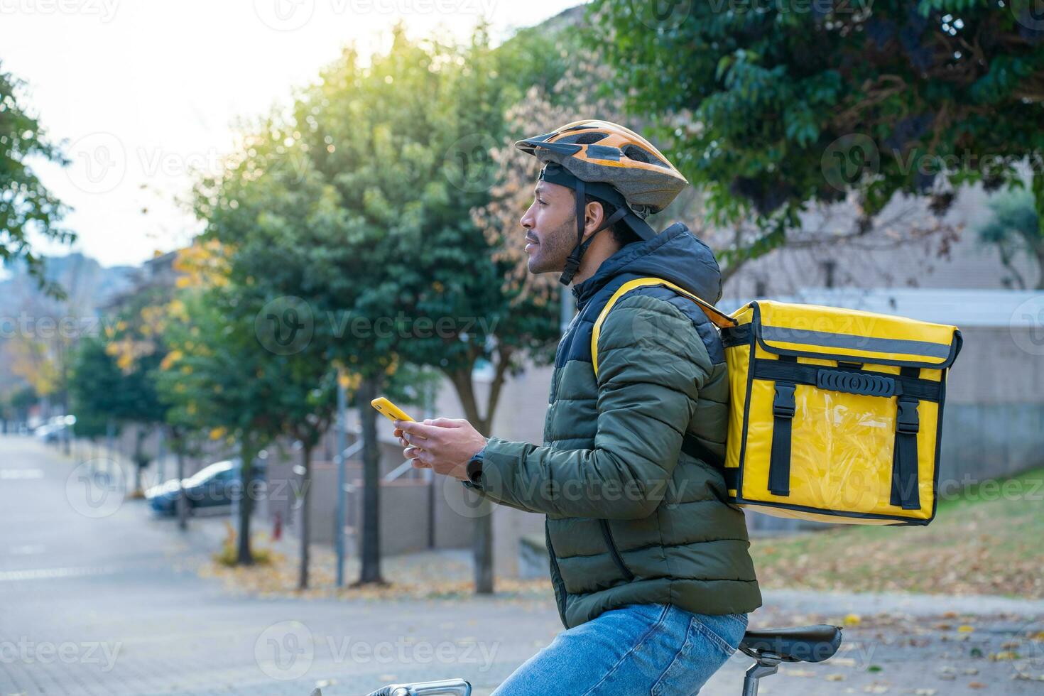 Delivery man on bike looking GPS location in the phone. Black courier delivering food and drink. photo