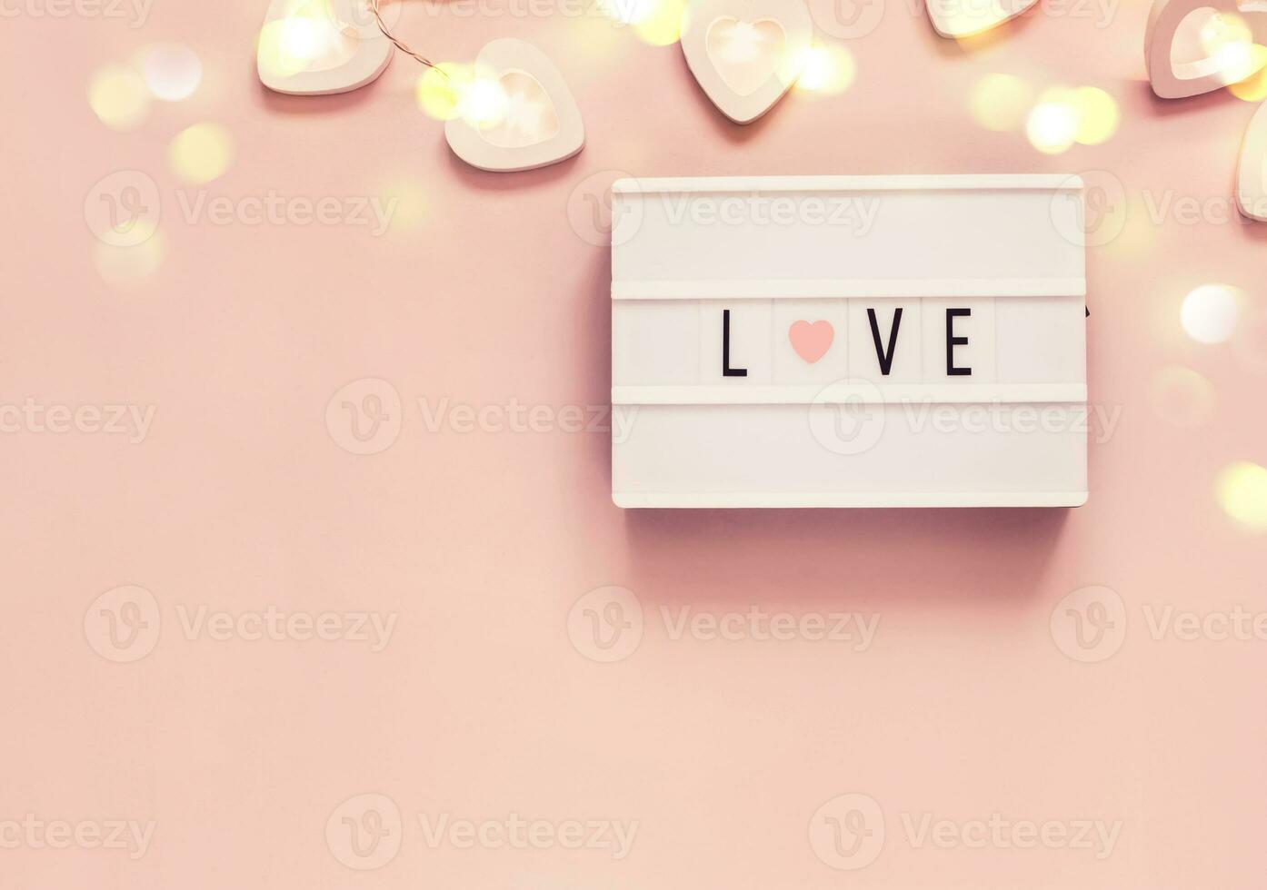 Pastel Valentine's day decoration with word love on lightboard and heart shape garland. Valentine's day or wedding party concept photo