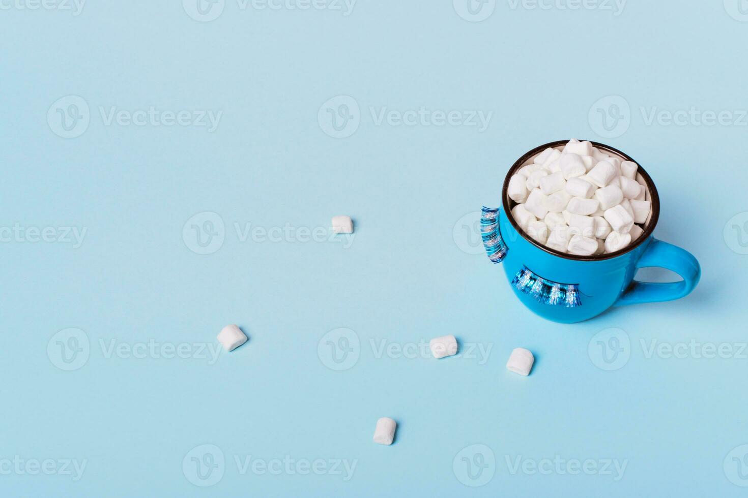 Blue monday concept. Blue mug of cocoa with marshmallows on blue background. Mug is decorated with eyelashes down photo