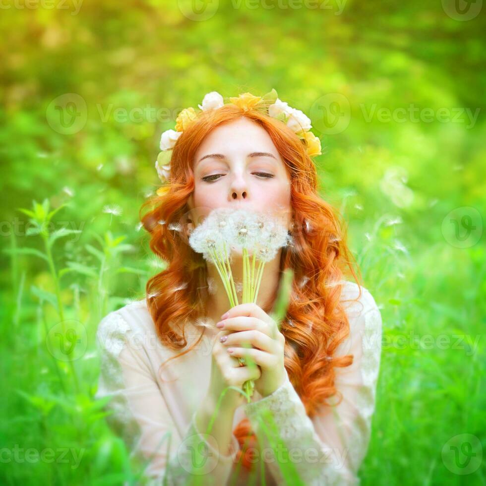Beautiful female blowing on a dandelion flowers photo