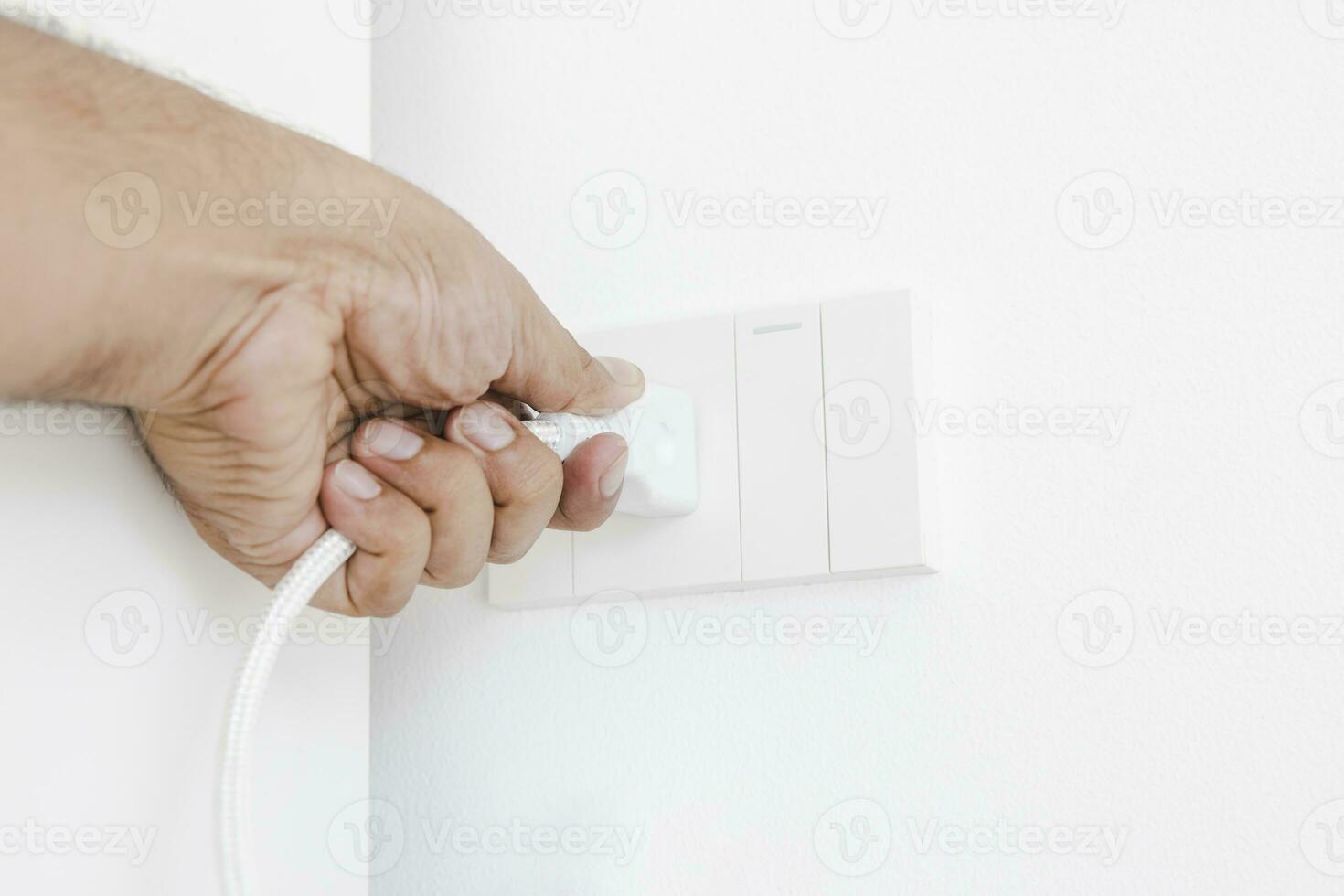 Hand plugging in an electrical appliance on white wall. Plug studio apartment power supply. Light switch. Power outlet. Concept of technology, connection, power saving, energy saving. photo