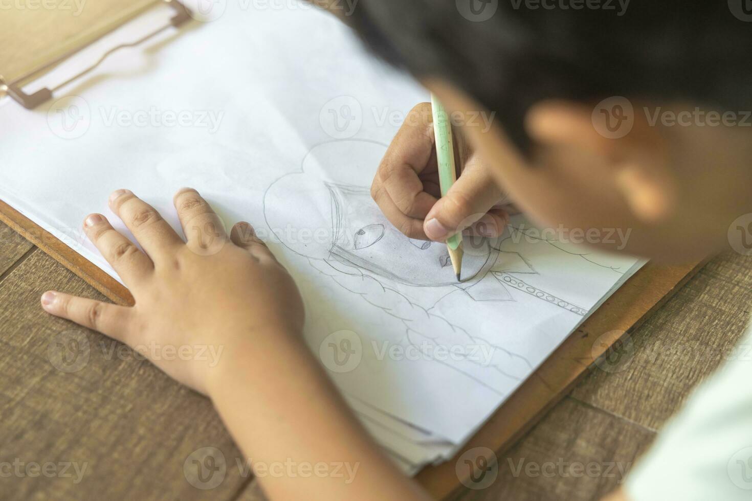 Close up portrait of Asian boy with black bangs, black eyes with a smiling face wearing a light green and lying on the floor of his house drawing a picture of a girl with braids. Education concept. photo