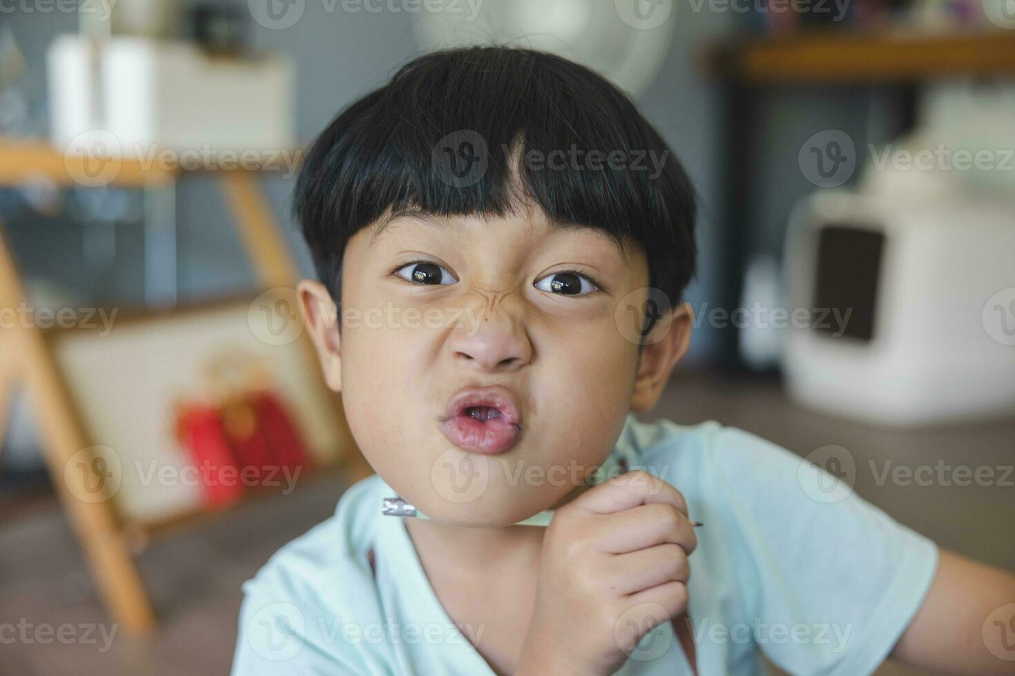 Close up portrait of Asian boy with black bangs, black eyes with a smiling face wearing a light green shirt look at camera and sitting on the floor of his house and hand holding pencil to draw. photo