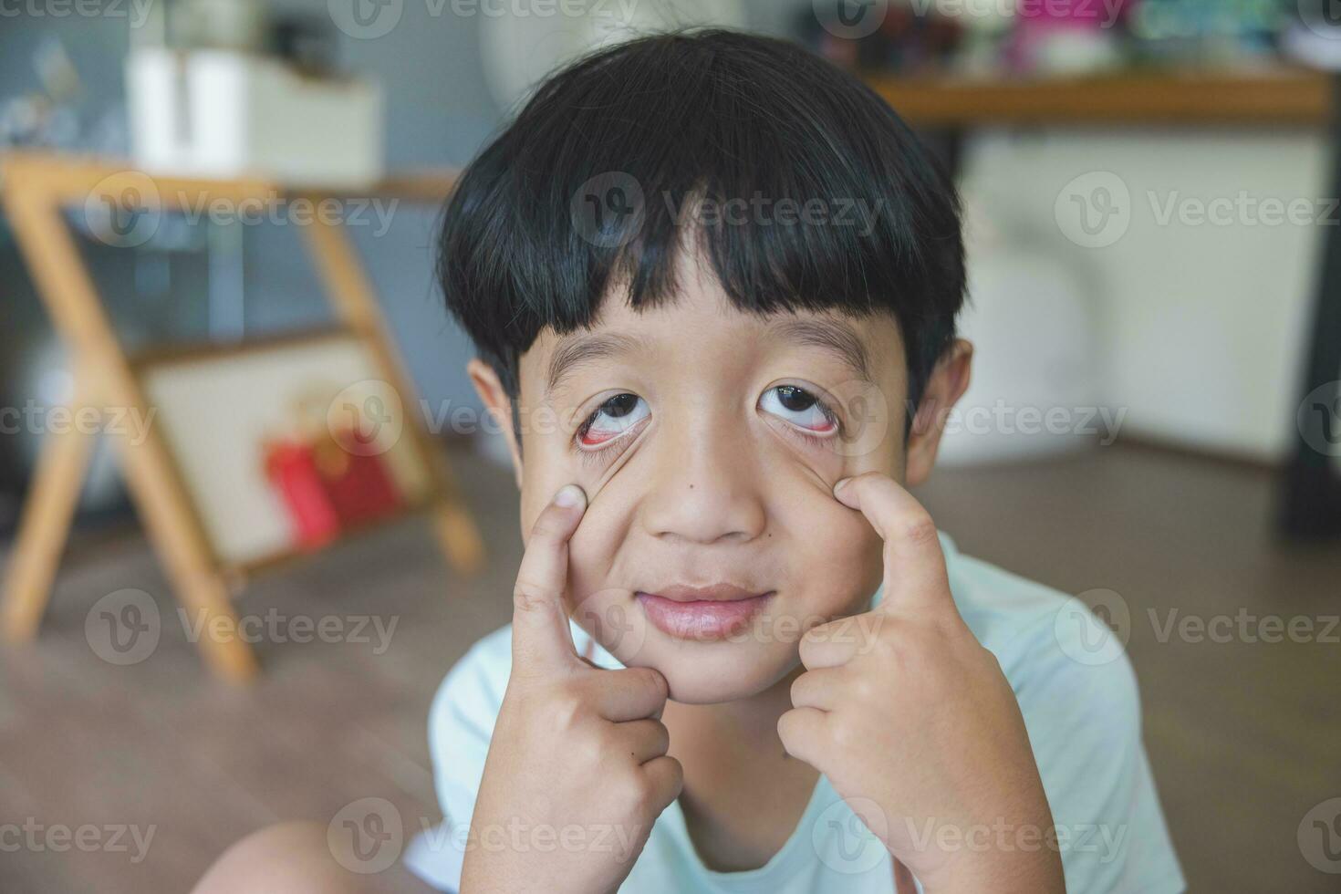 Close up portrait of Asian boy with black bangs, black eyes with a smiling face wearing a light green shirt look at camera and sitting on the floor of his house and hand holding pencil to draw. photo