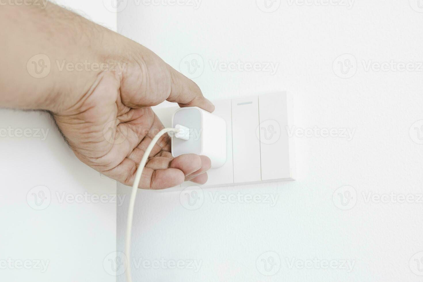 Hand plugging in an electrical appliance on white wall. Plug studio apartment power supply. Light switch. Power outlet. Concept of technology, connection, power saving, energy saving. photo