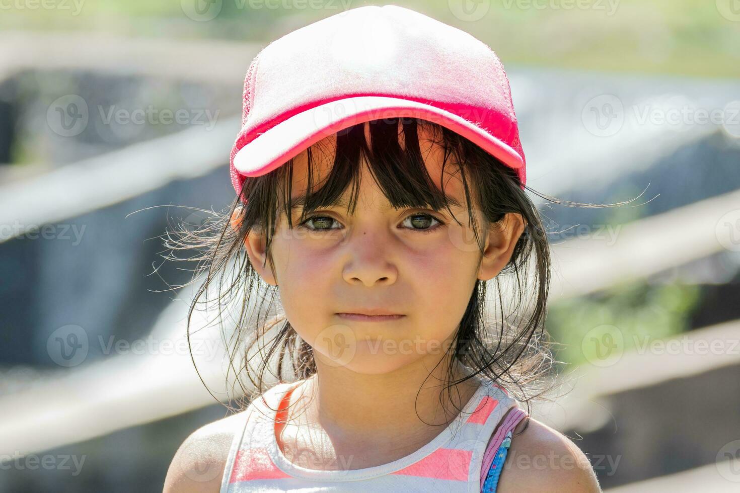 muy cerca retrato de un latín niño en un viaje. el niña usa un rosado gorra. ella mira a el cámara con un muy grave rostro. foto