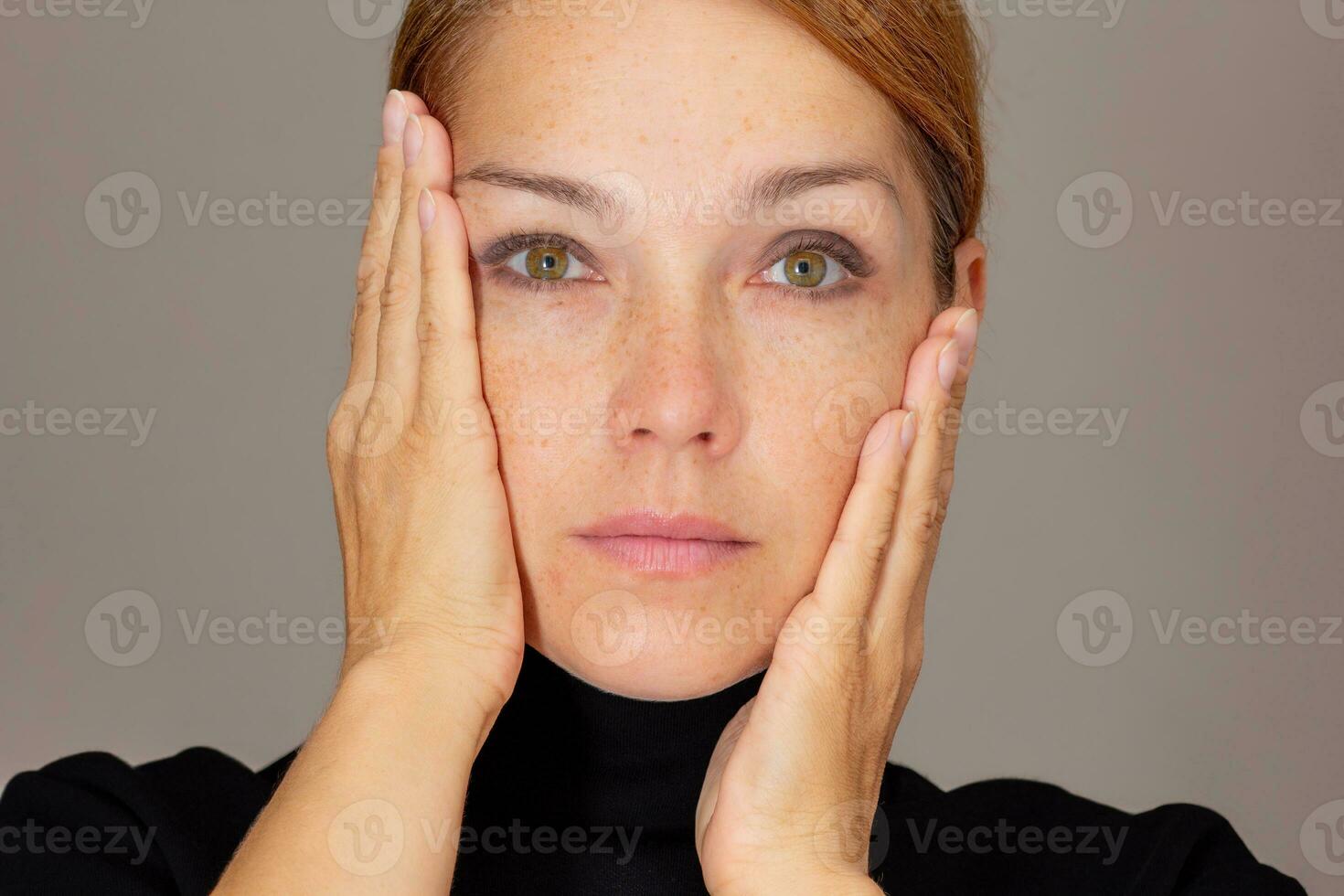 Portrait woman looking at camera holding palms on cheeks surprised of soft skin photo