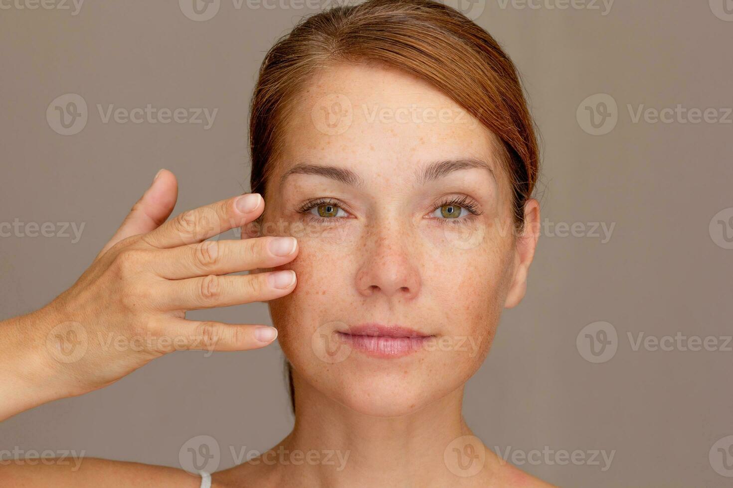 Portrait of cropped caucasian middle aged woman face with freckles holding fingers on cheek photo