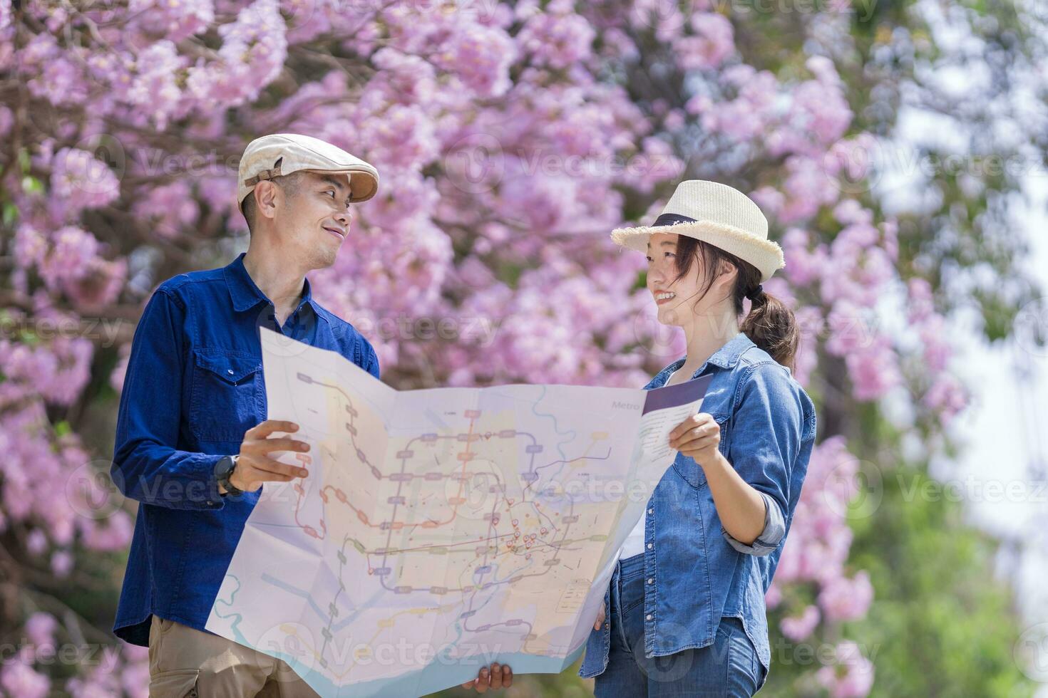 Asian couple tourist holding city map while walking in the park at cherry blossom tree during spring sakura flower festival photo