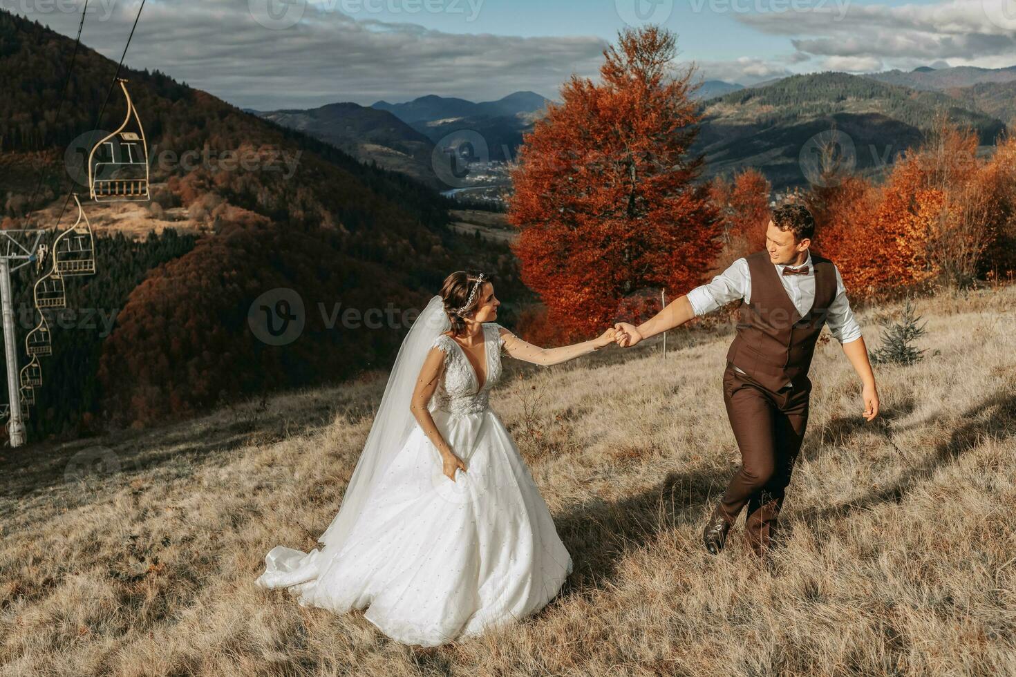 Wedding couple walks in the mountains. The groom leads the bride by the hand. The dress of the bride develops in the wind. photo