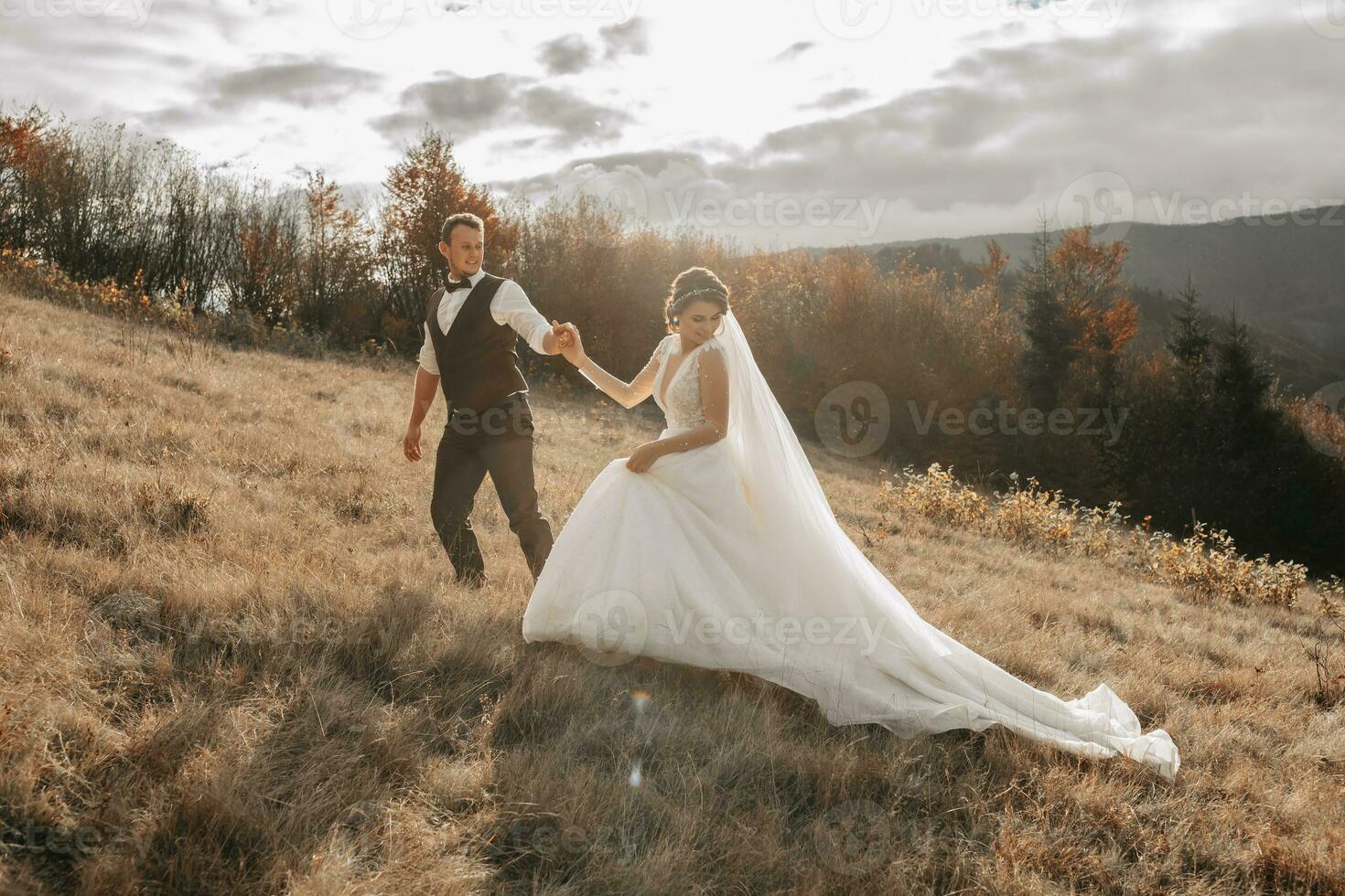 Wedding couple walks in the mountains. The groom leads the bride by the hand. The dress of the bride develops in the wind. photo