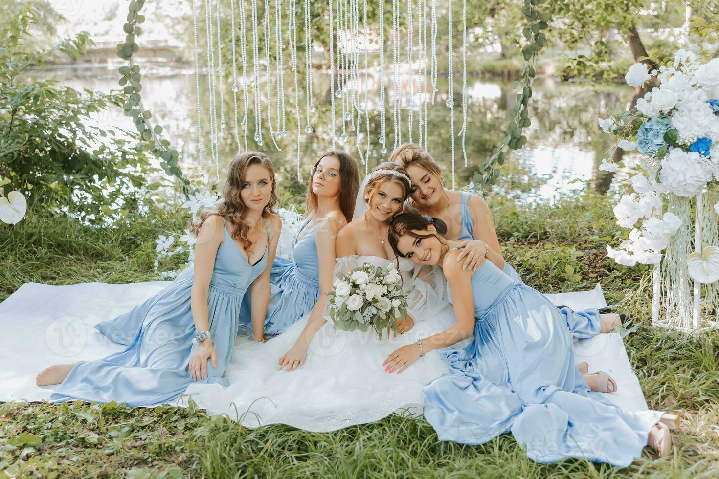 The bridesmaids are in blue dresses, the bride is holding a beautiful bouquet. Sitting enjoying the celebration. Beautiful luxury wedding blog concept. Spring wedding. photo