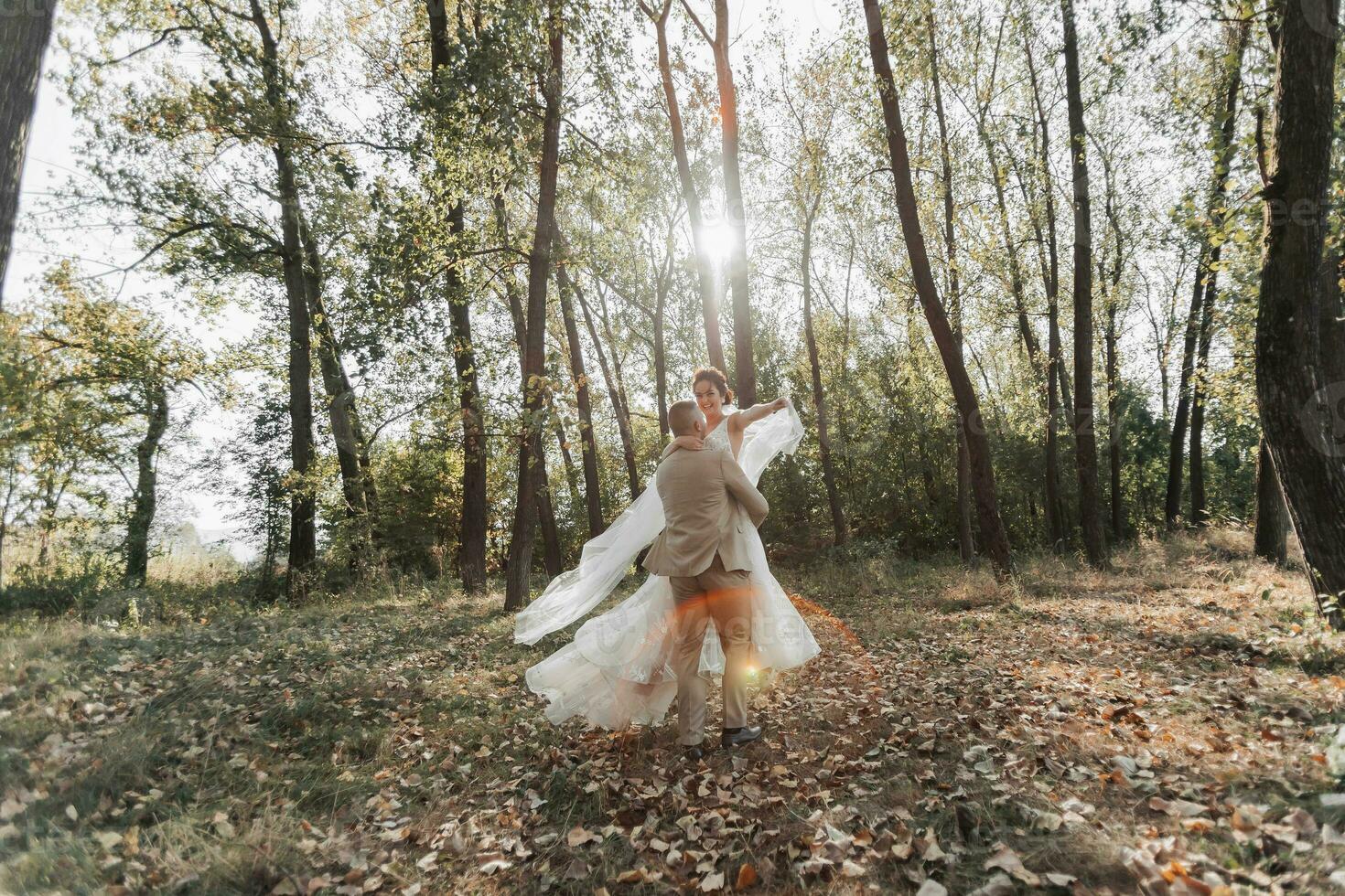 retrato de contento novia y novio en el bosque. el novio sostiene el novia en su brazos, bailando con su. un largo velo en el aire. un rayo de el Dom en el foto. amplio ángulo foto