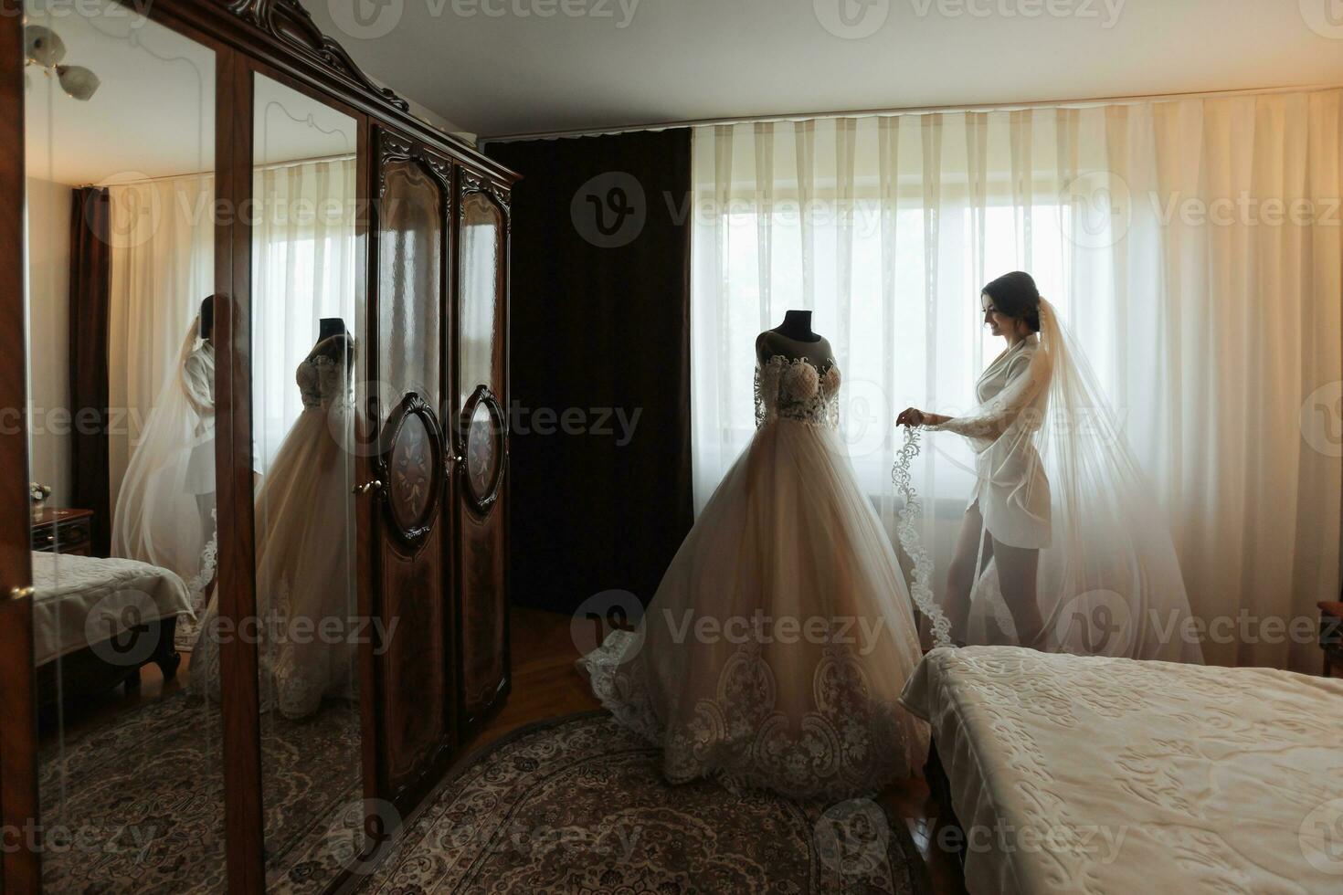 Brunette bride in a robe, posing for the camera, looking at her wedding  dress. Elegant hairstyle. Nice makeup. Voluminous veil. Morning of the  bride 36409244 Stock Photo at Vecteezy