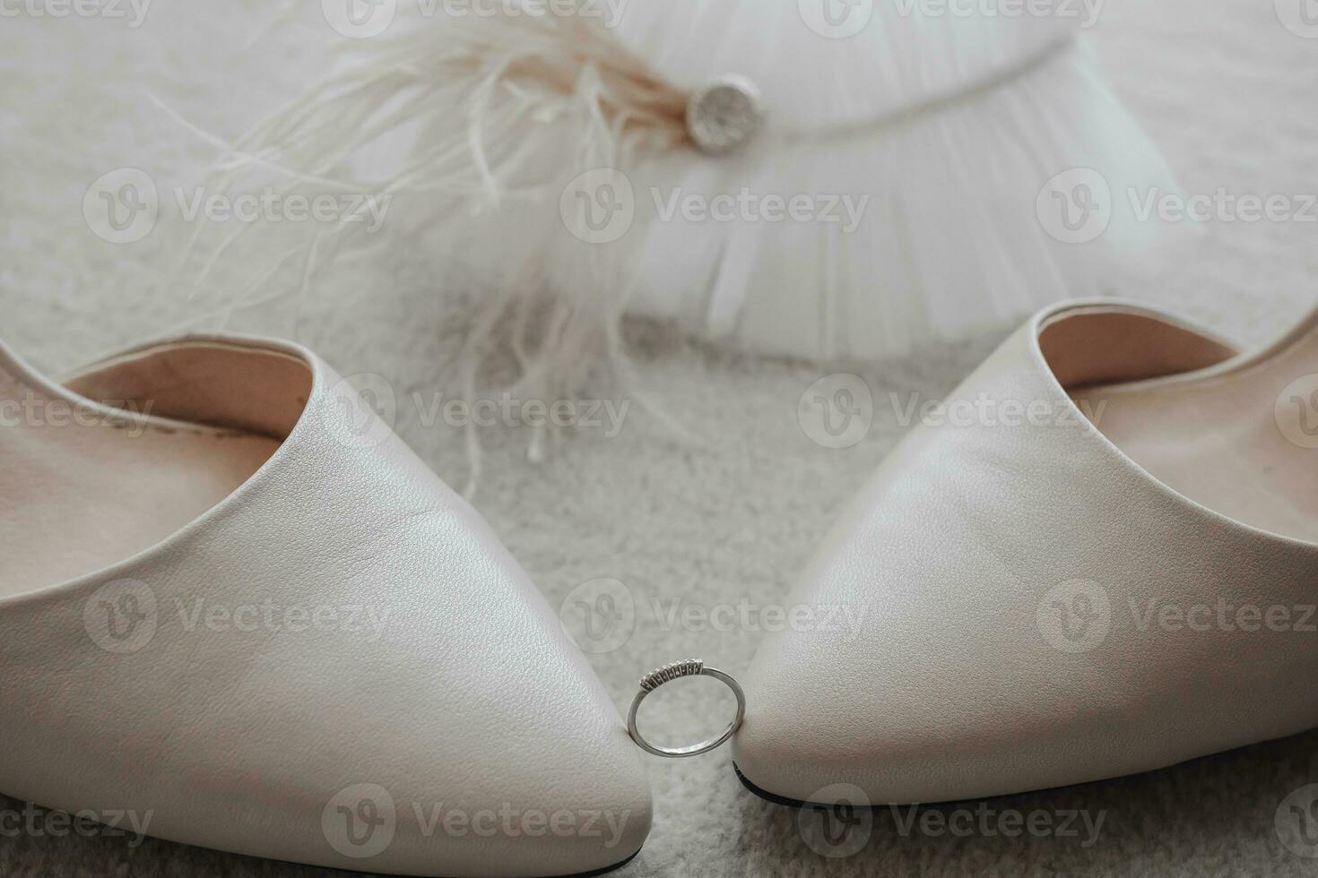 The wedding ring is held by the tips of the shoes, behind the garter is decorated with feathers, on a gray background photo