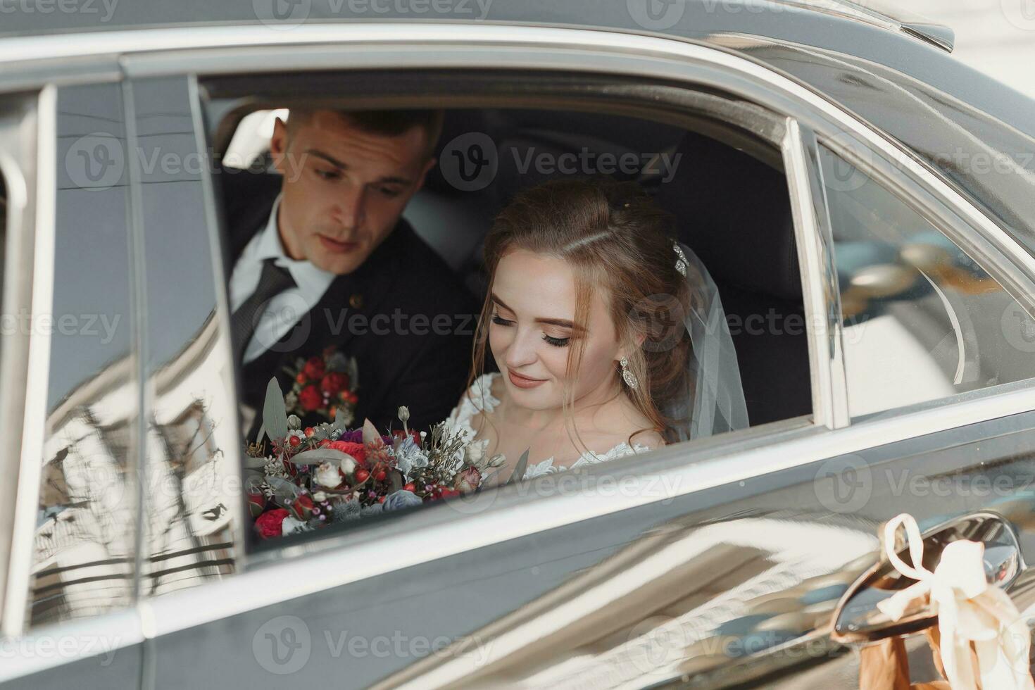 A modern bride and groom in a lace dress in a car window. Beautiful and smiling newlyweds. Happy holiday. photo