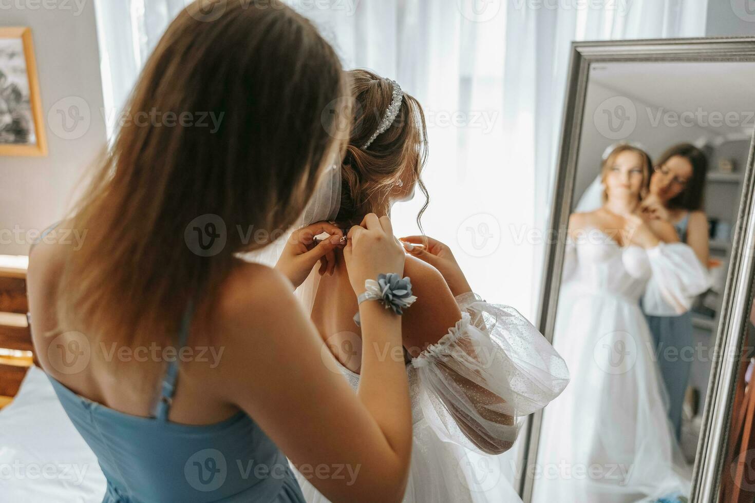 The bride's friend helps in the morning, fastens a chain with a pendant with a boutonniere on her hand, the bride has a beautiful hairstyle and light natural makeup. Wedding portrait. photo